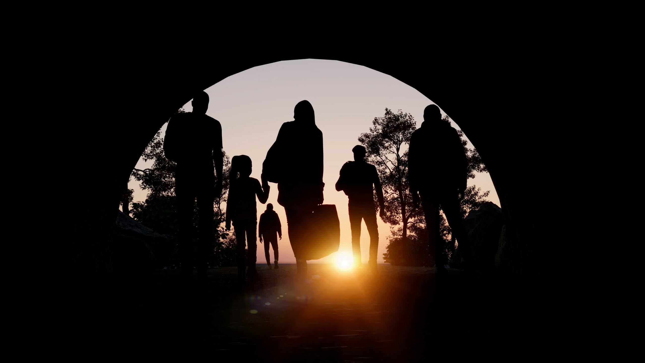 Siluetas de un grupo caminando bajo un arco al atardecer, con árboles visibles y un cálido resplandor al fondo.