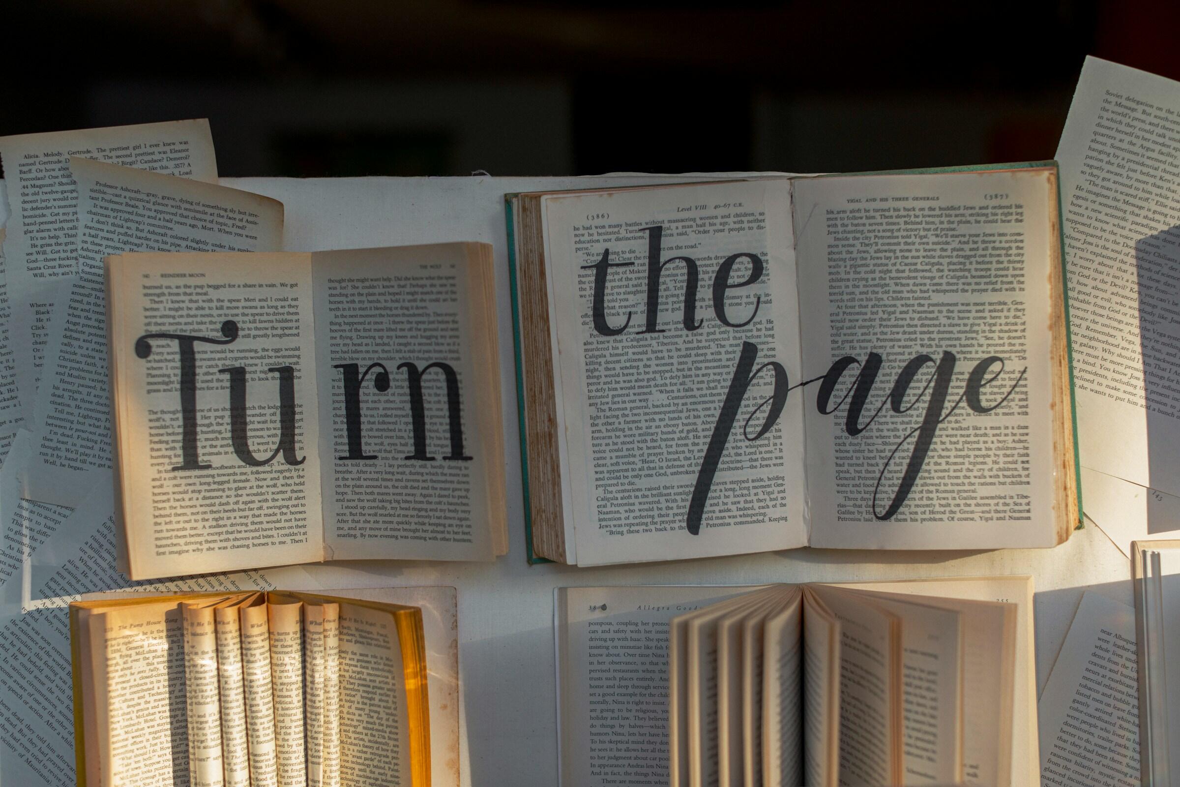 Una muestra artística de libros abiertos con las palabras «Turn the page» (Pasa la página) en una elegante tipografía, rodeadas de páginas adicionales.