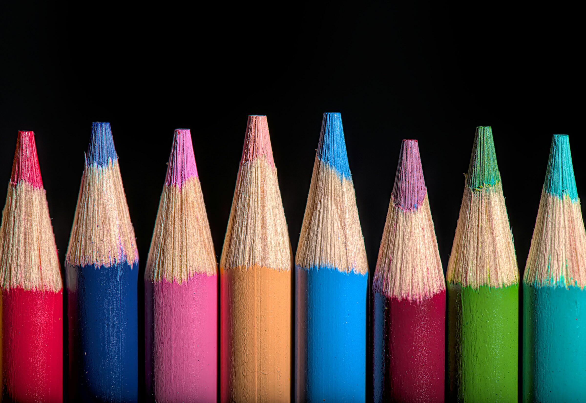 Primer plano de puntas de lápices afilados de colores dispuestos en fila, sobre un fondo oscuro, que muestran vibrantes tonos de rojo, azul, rosa y verde.