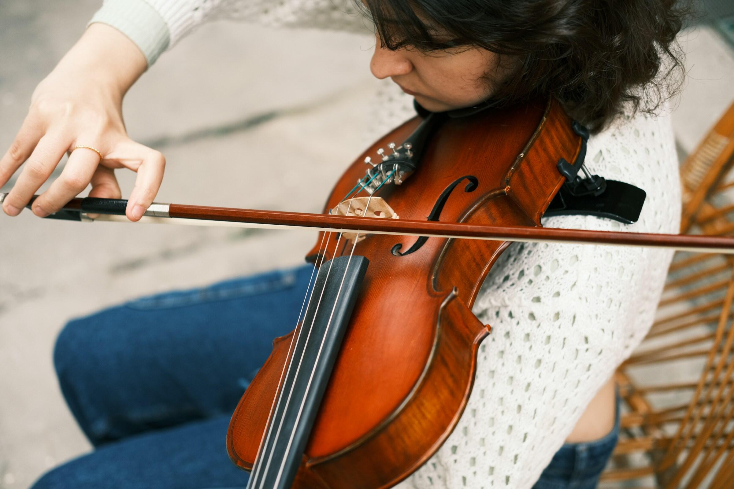 Primer plano de una persona tocando el violín, centrándose en su mano que sujeta el arco contra la madera pulida del instrumento.