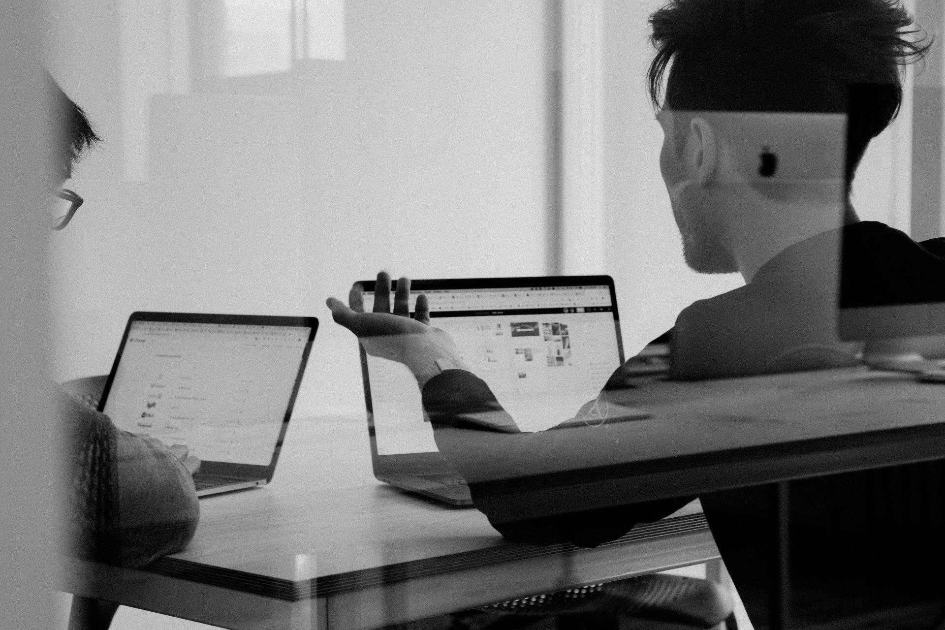 Dos individuos en una mesa, cada uno usando su computadora portátil.