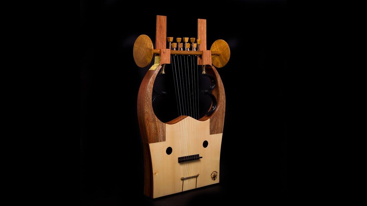 Guitarra única con un cuerpo de madera que se asemeja a un rostro antropomórfico, seis cuerdas y clavijas de afinación en forma de cuerno sobre un fondo negro. Artística y caprichosa.