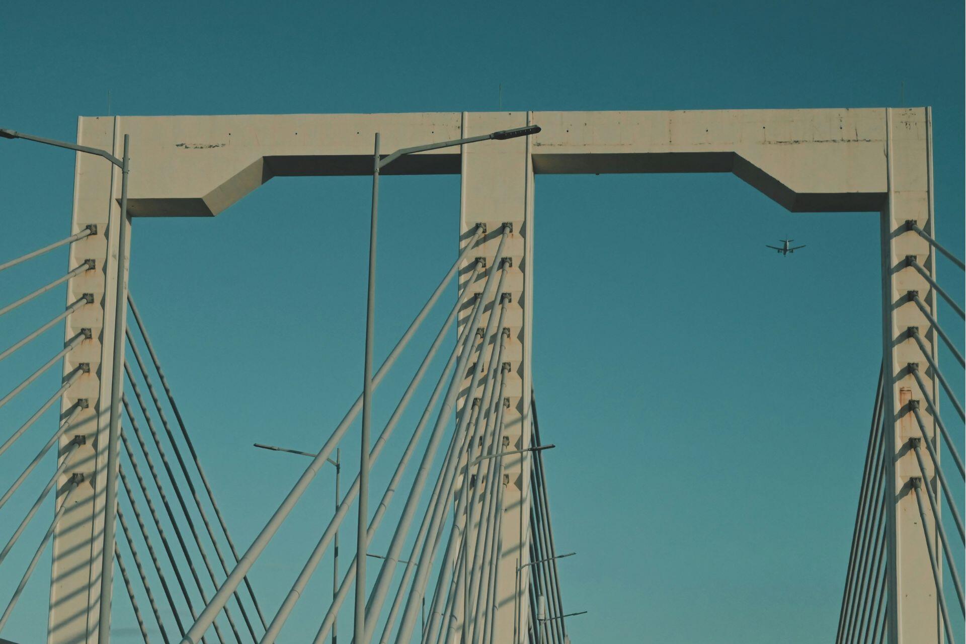 Un avión vuela sobre un puente donde circula un automóvil.