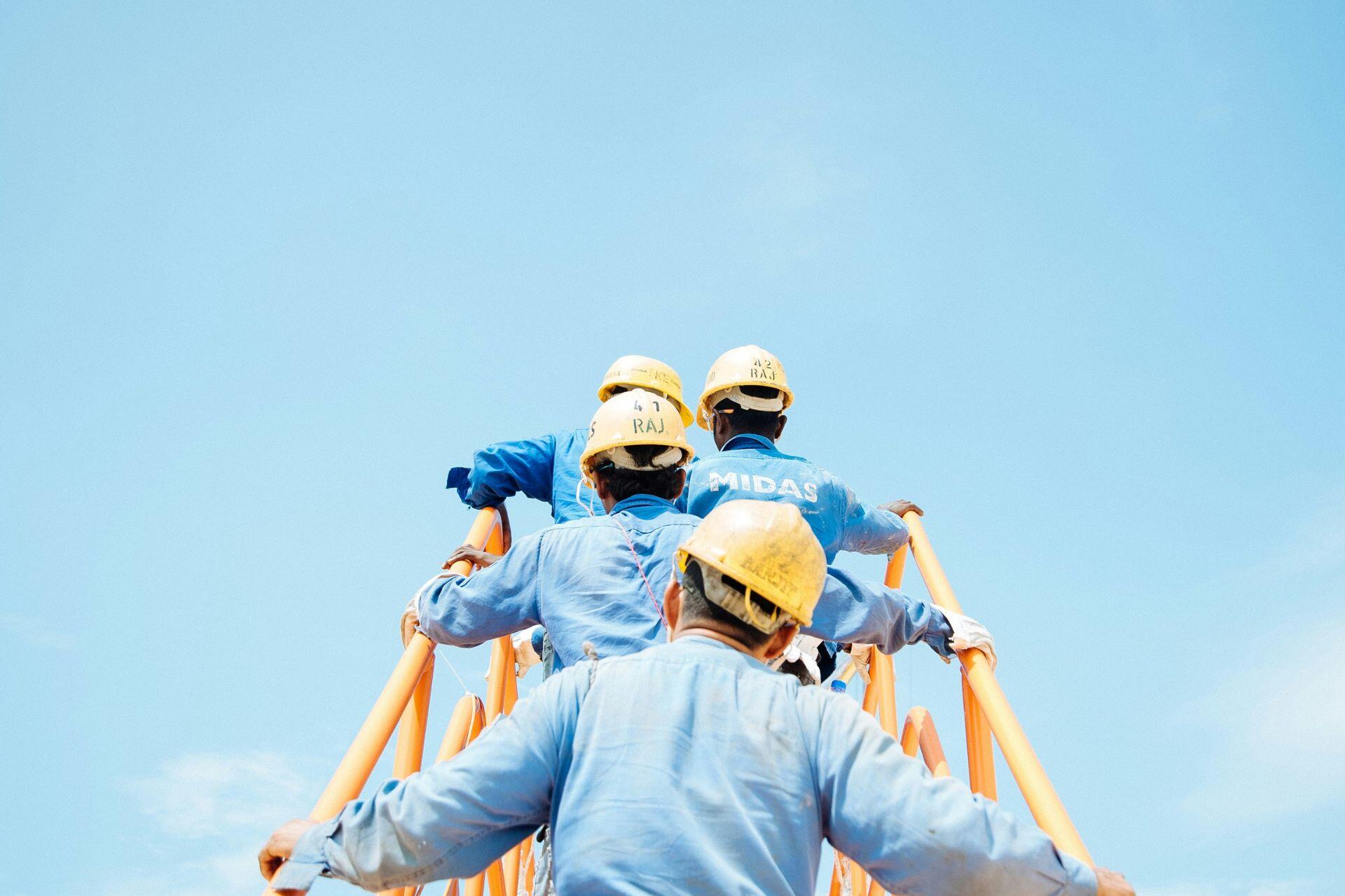 Cuatro hombres con overoles azules subiendo una escalera.