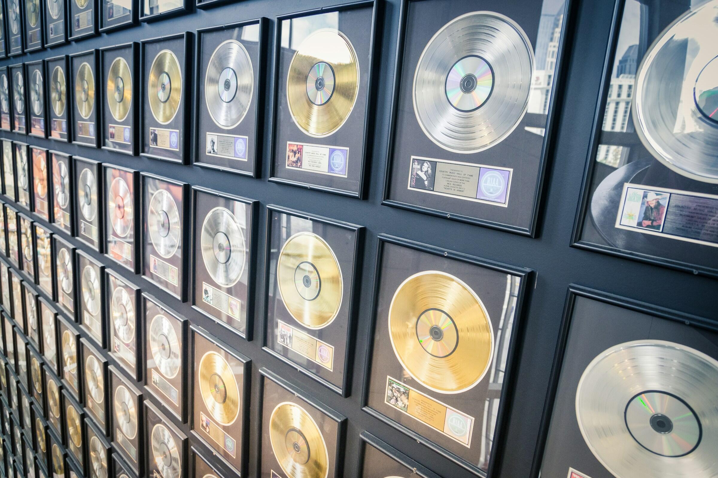 Una exposición mural con numerosos discos de oro y platino enmarcados, que muestra los logros de varios artistas musicales.