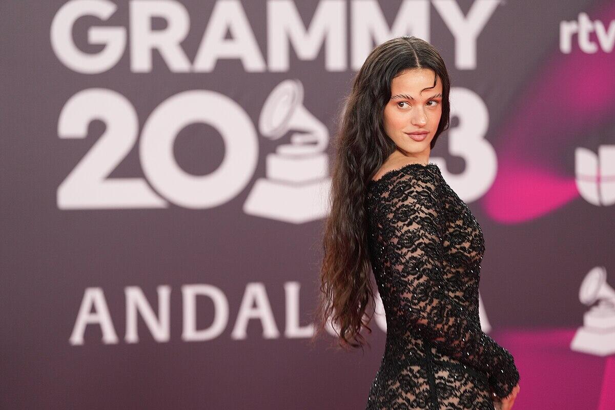 la cantante rosalia con un vestido de encaje negro posa en la alfombra roja de los premios Grammy 2023, con un glamuroso telón de fondo.
