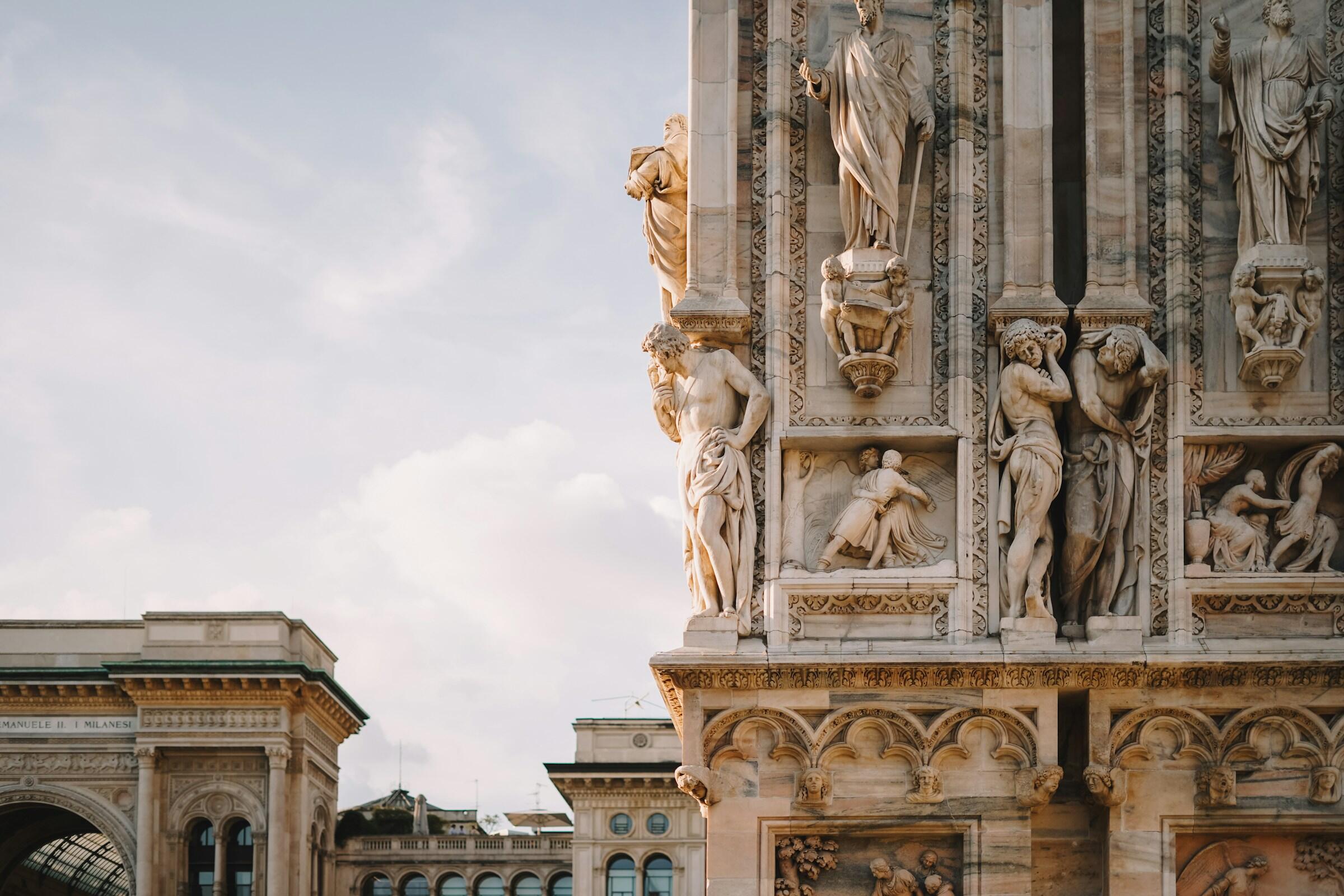 Ornamentadas tallas de piedra adornan un edificio histórico, mostrando figuras y detalles intrincados contra un cielo suave y nublado.