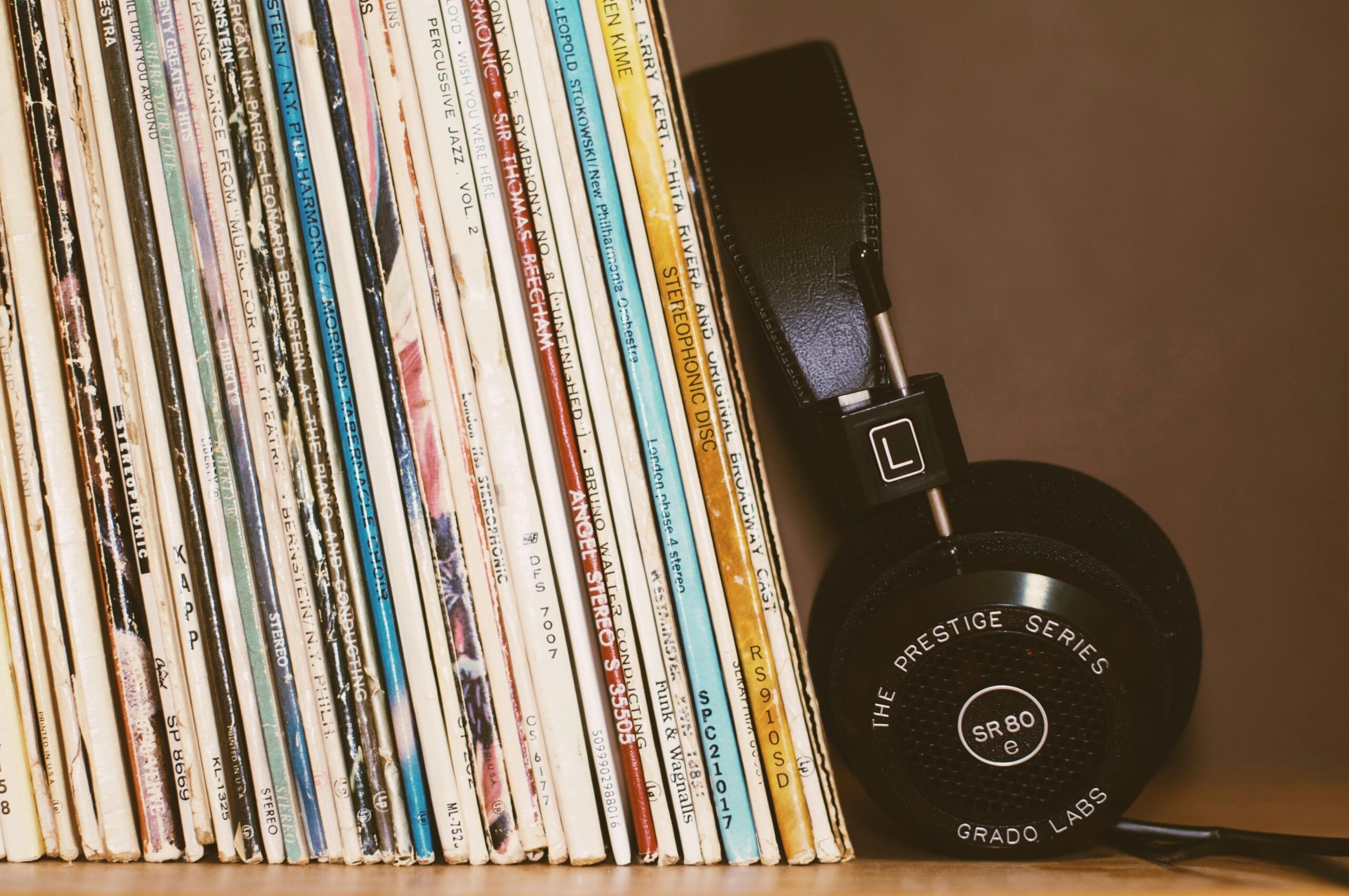 Un par de auriculares Grado Labs SR80 descansa junto a una colección de discos de vinilo antiguos en una estantería de madera.