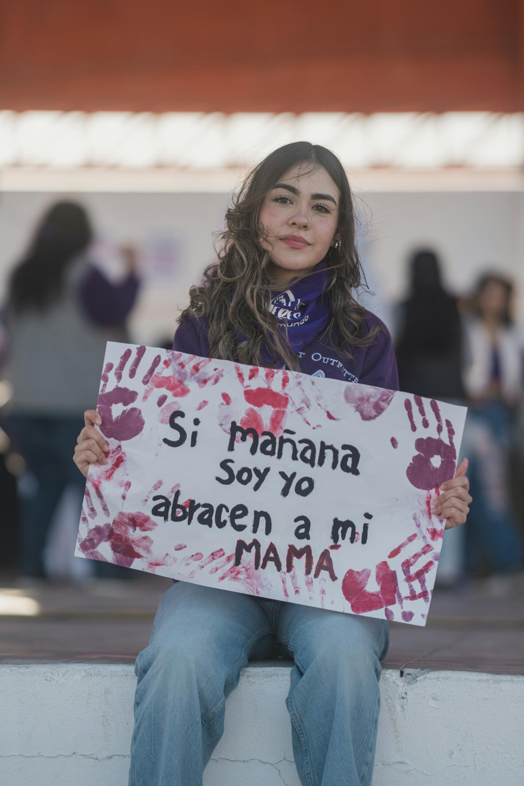 Una persona sostiene un cartel con huellas de manos en el que se lee «Si mañana soy yo, abracen a mi MAMA», en defensa de la concienciación y la protección materna.