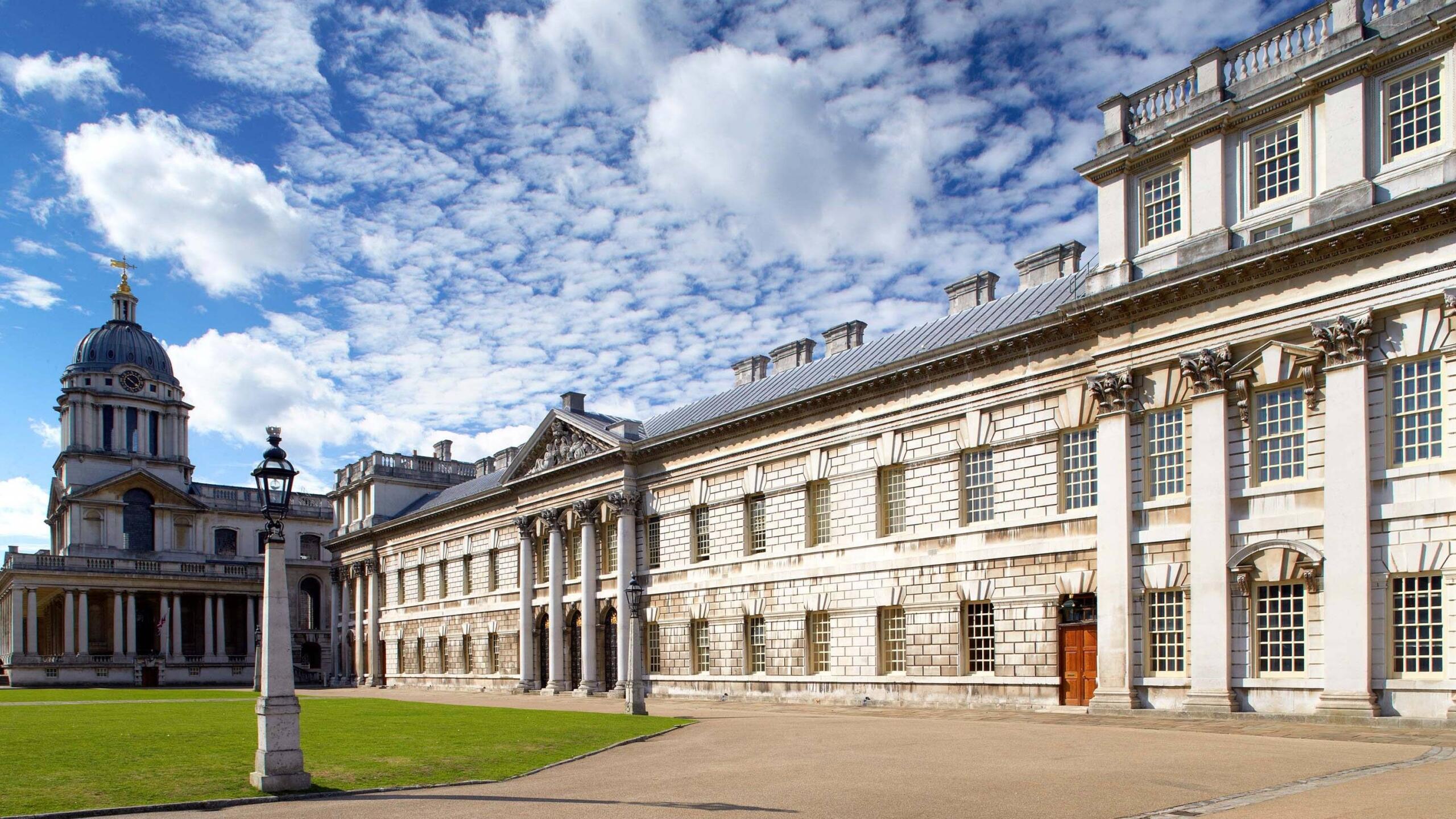 Gran edificio histórico con columnas clásicas y detallados trabajos en piedra bajo un cielo salpicado de nubes esponjosas; estructura abovedada visible al fondo.