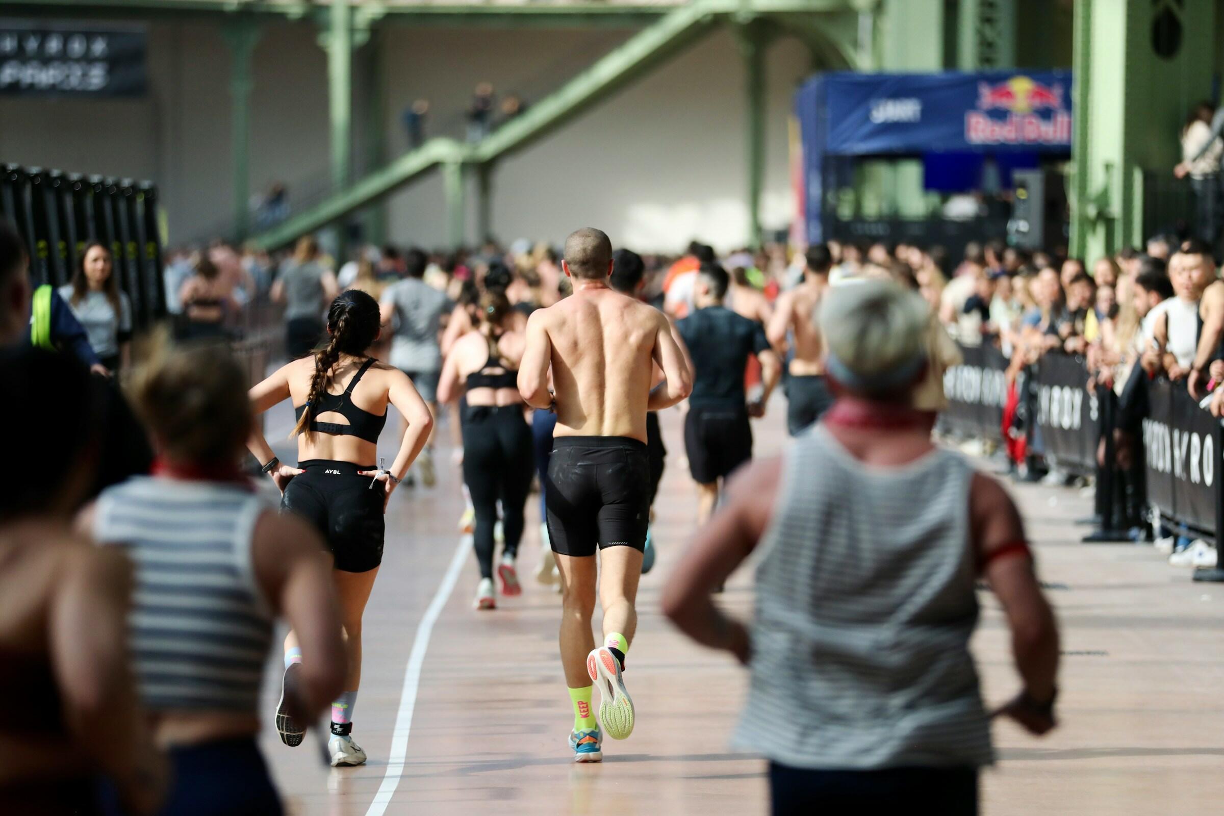 Corredores que participan en una carrera en pista cubierta con espectadores que observan desde detrás de las vallas a ambos lados de la pista.