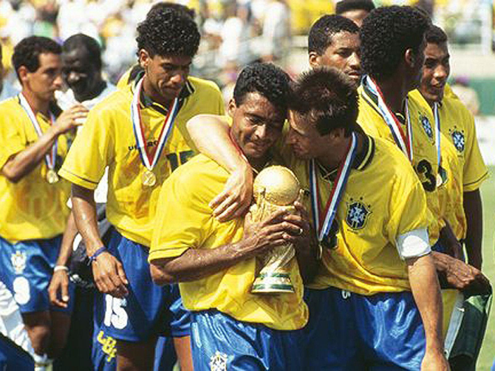 Los futbolistas brasileños celebran con una sonrisa, sosteniendo el trofeo de la Copa del Mundo. Visten camisetas amarillas y medallas, lo que transmite alegría y triunfo.