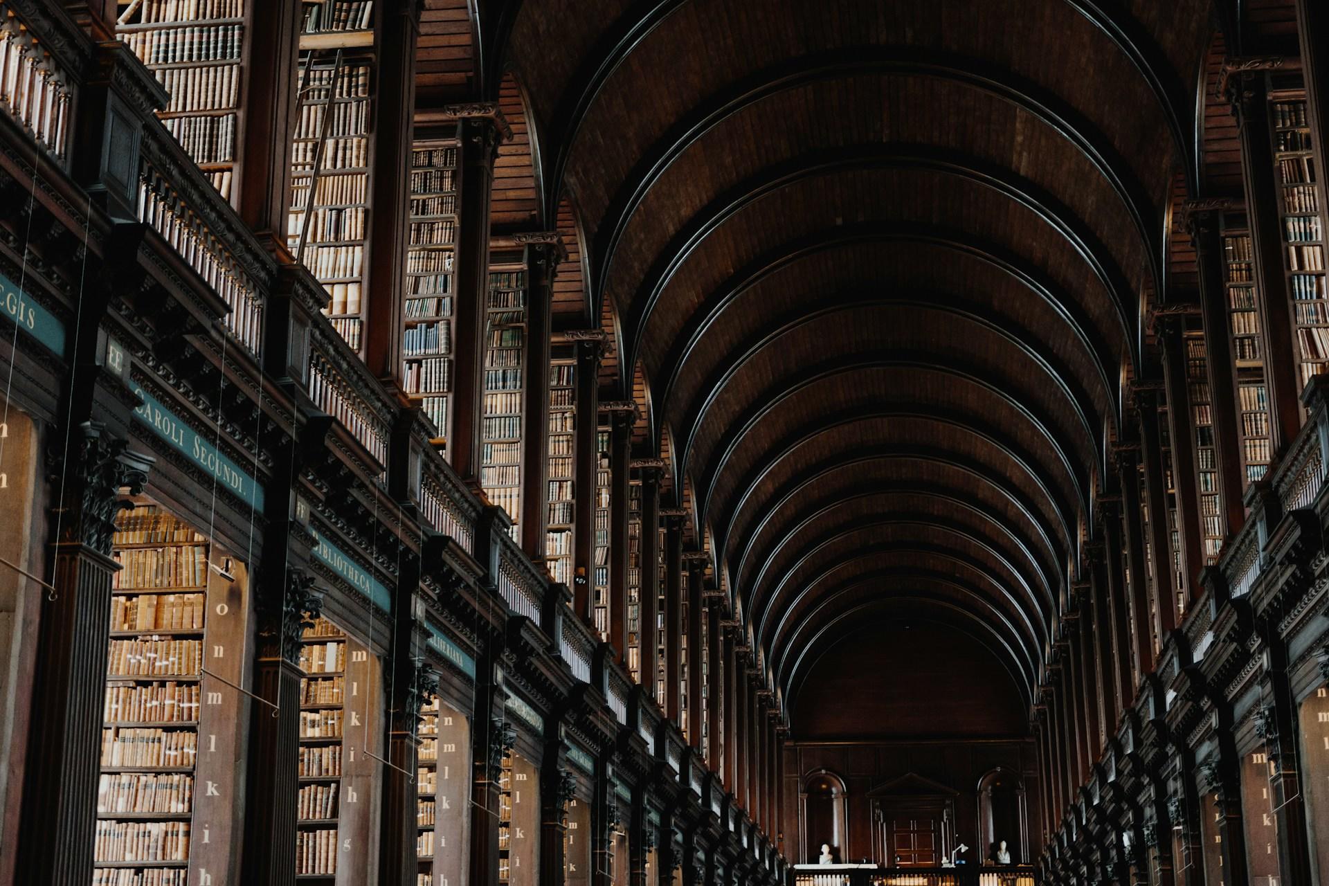 Interior de una gran biblioteca histórica con imponentes estanterías de madera y un alto techo abovedado que se extiende a lo largo de un pasillo.