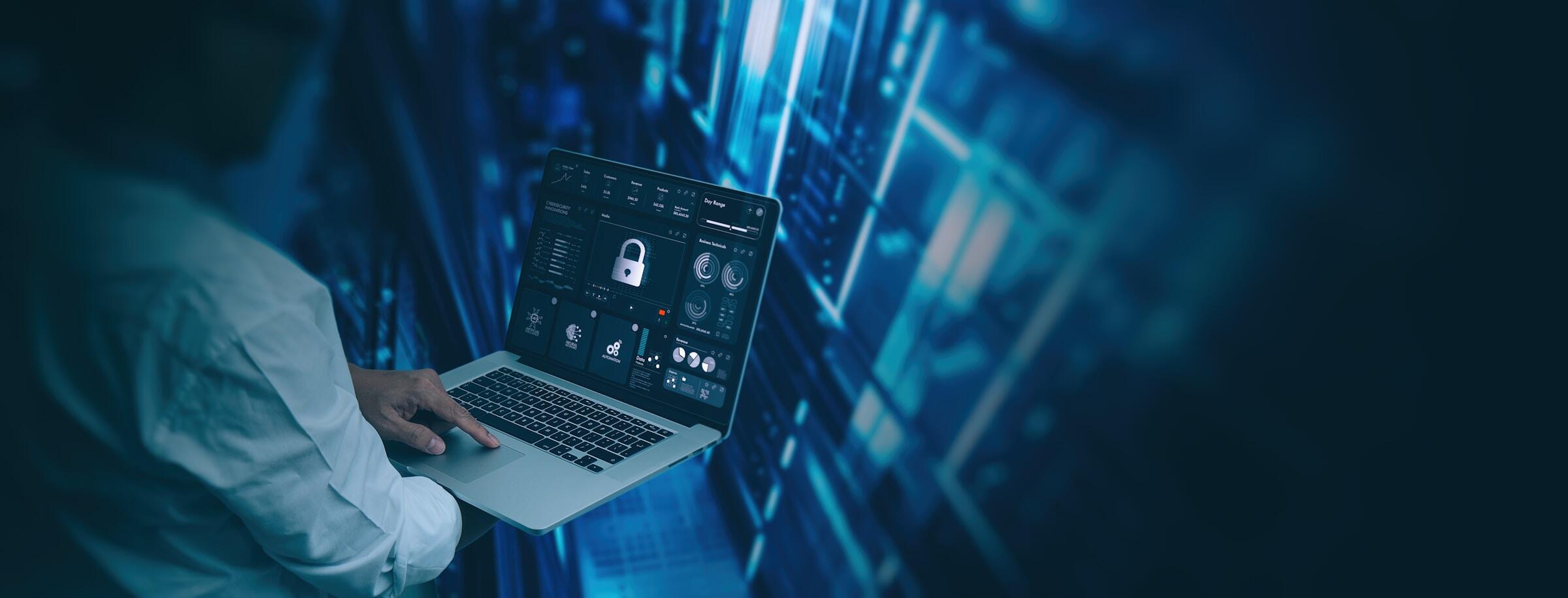 Persona con un ordenador portátil en el que se ve un panel de control de ciberseguridad con un icono de candado, supervisando datos en una sala de servidores con iluminación azul.