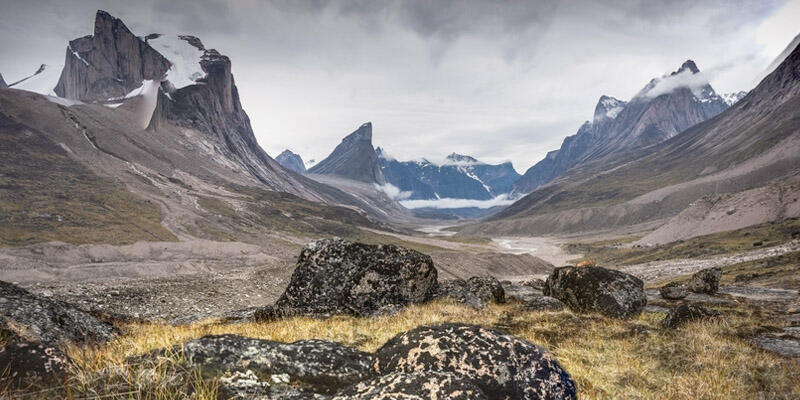 Un extenso valle rocoso rodeado de imponentes montañas nevadas bajo un cielo nublado. El paisaje transmite una sensación de aislamiento y grandeza.