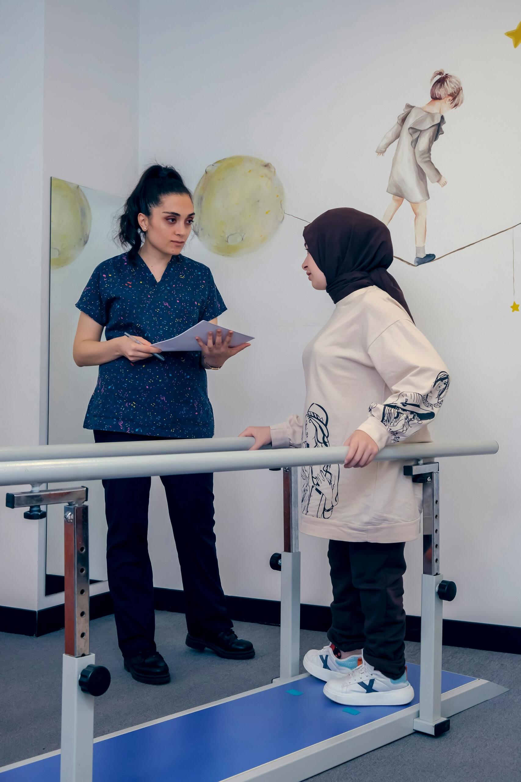 Un profesional sanitario examina a una paciente joven que lleva un hiyab durante un ejercicio de marcha de fisioterapia en una sala decorada.
