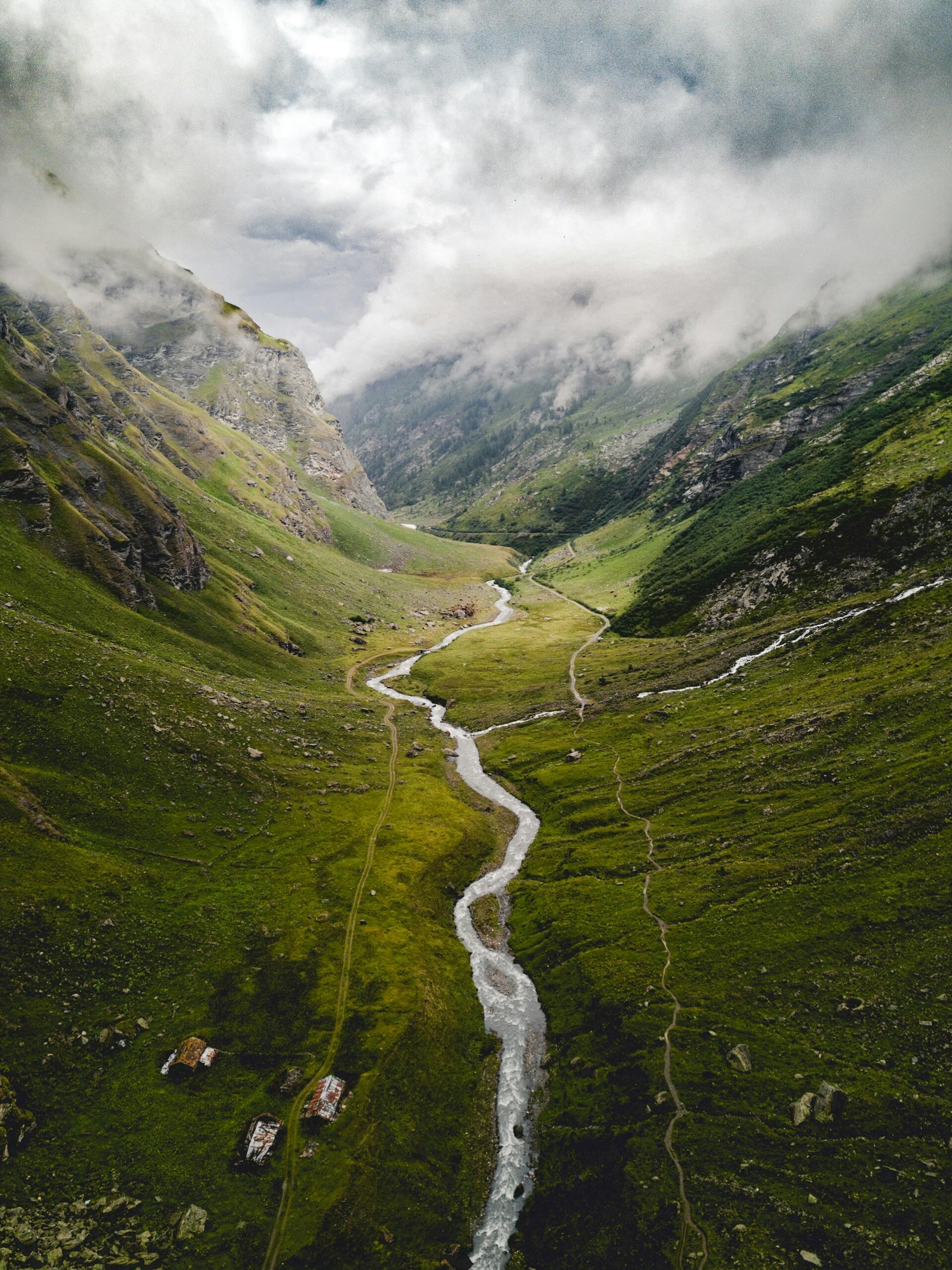 Vista aérea de un río serpenteante que atraviesa exuberantes montañas verdes bajo un cielo nublado. La escena transmite tranquilidad y belleza natural.