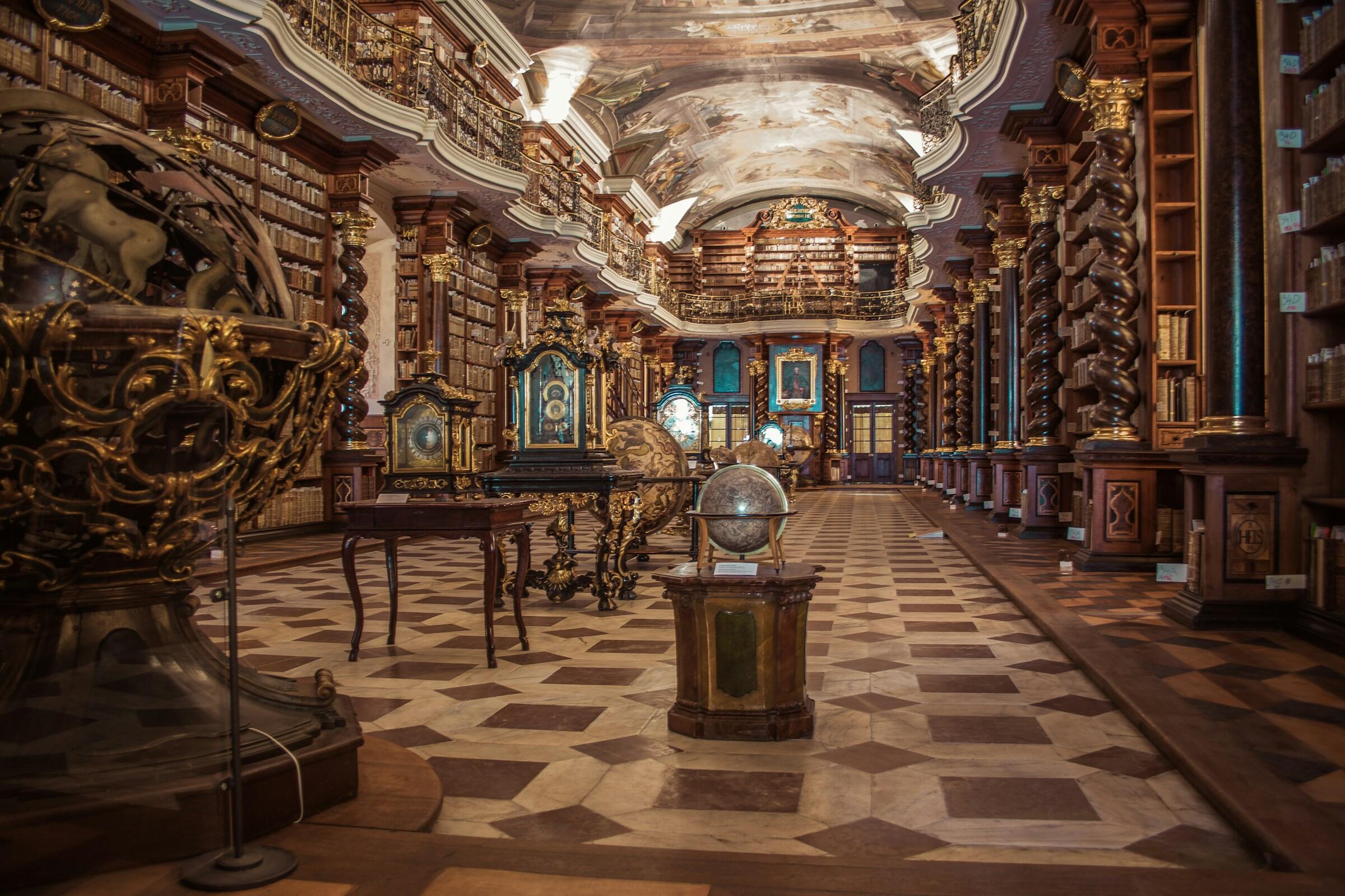 Interior de una biblioteca histórica ornamentada, con estanterías de madera, globos terráqueos, una decoración intrincada y un techo pintado con gran detalle.
