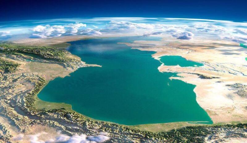 Vista satelital del mar Caspio, rodeado de tierras áridas y terrenos rocosos, con nubes dispersas en la parte superior y una extensión de agua de un azul intenso en la parte inferior.