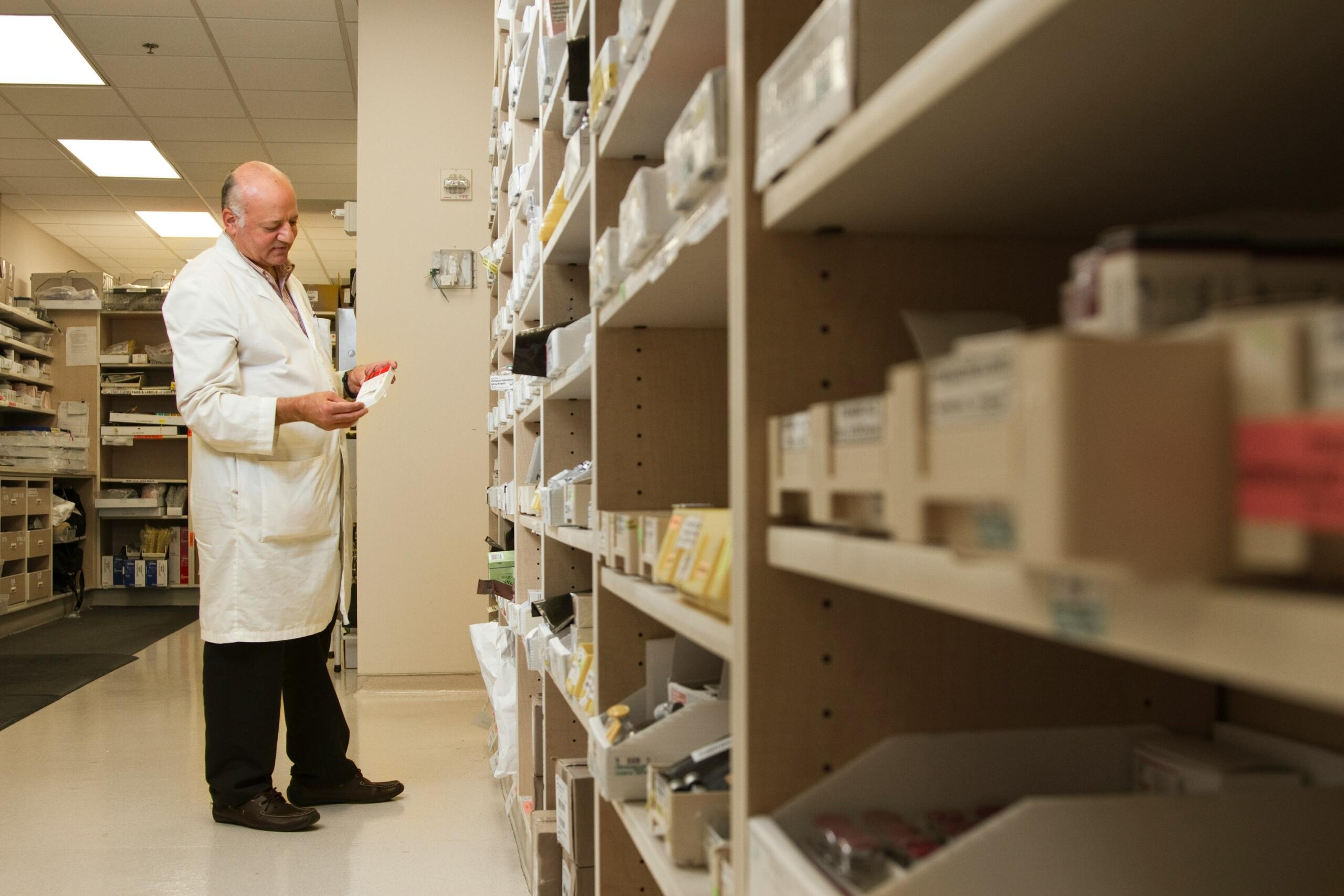 Un doctor con bata blanca seleccionando medicamentos de las estanterías en el almacén de un hospital bien organizado.