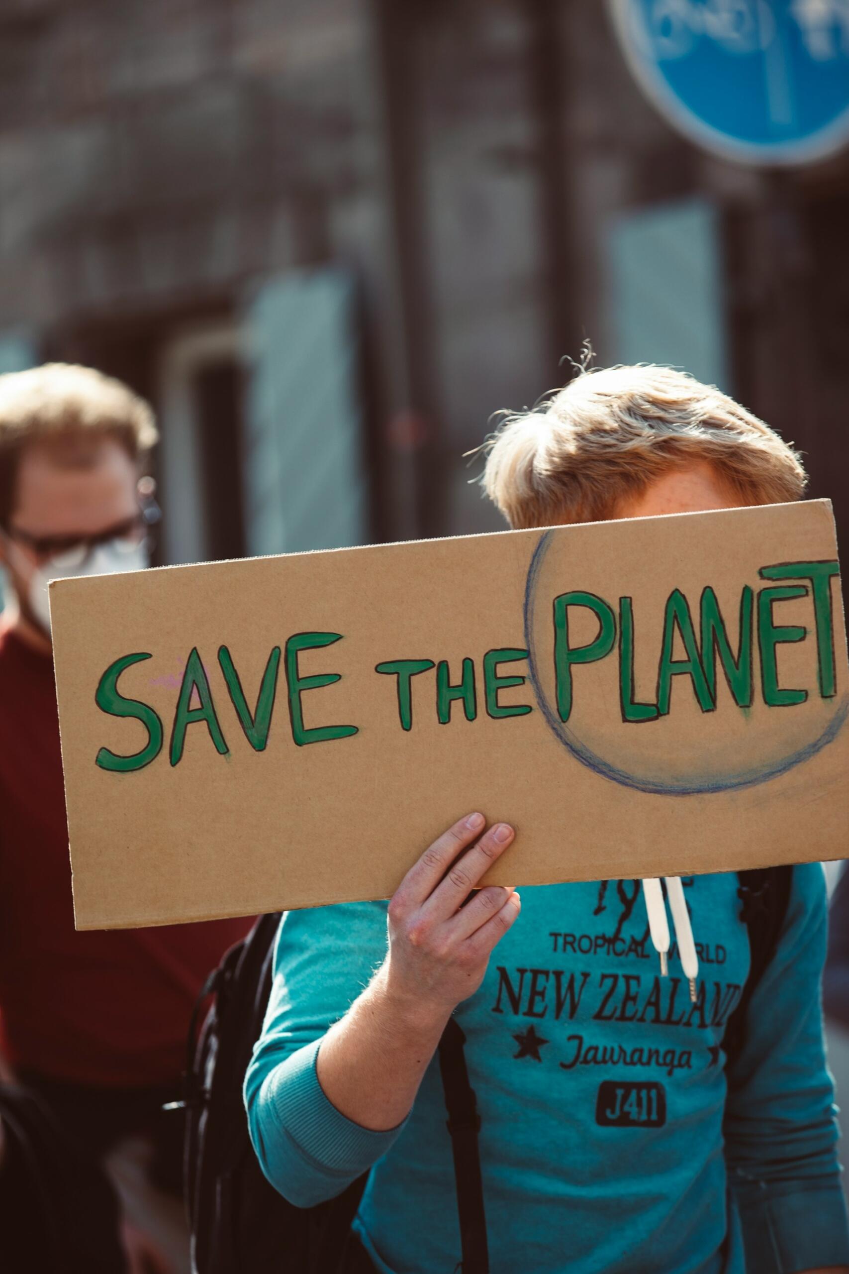 Una persona sostiene un cartel de cartón en el que se lee «Salvemos el planeta» durante una manifestación. La escena tiene lugar al aire libre y transmite un sentido de urgencia y preocupación por los problemas medioambientales.