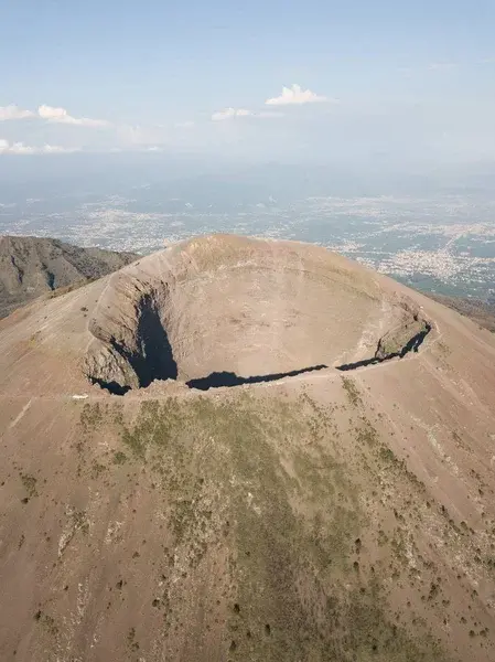 Vista aérea del cráter del Vesubio, con un terreno accidentado y árido y una vegetación escasa. El extenso paisaje y el cielo despejado crean una sensación de grandiosidad y amplitud.
