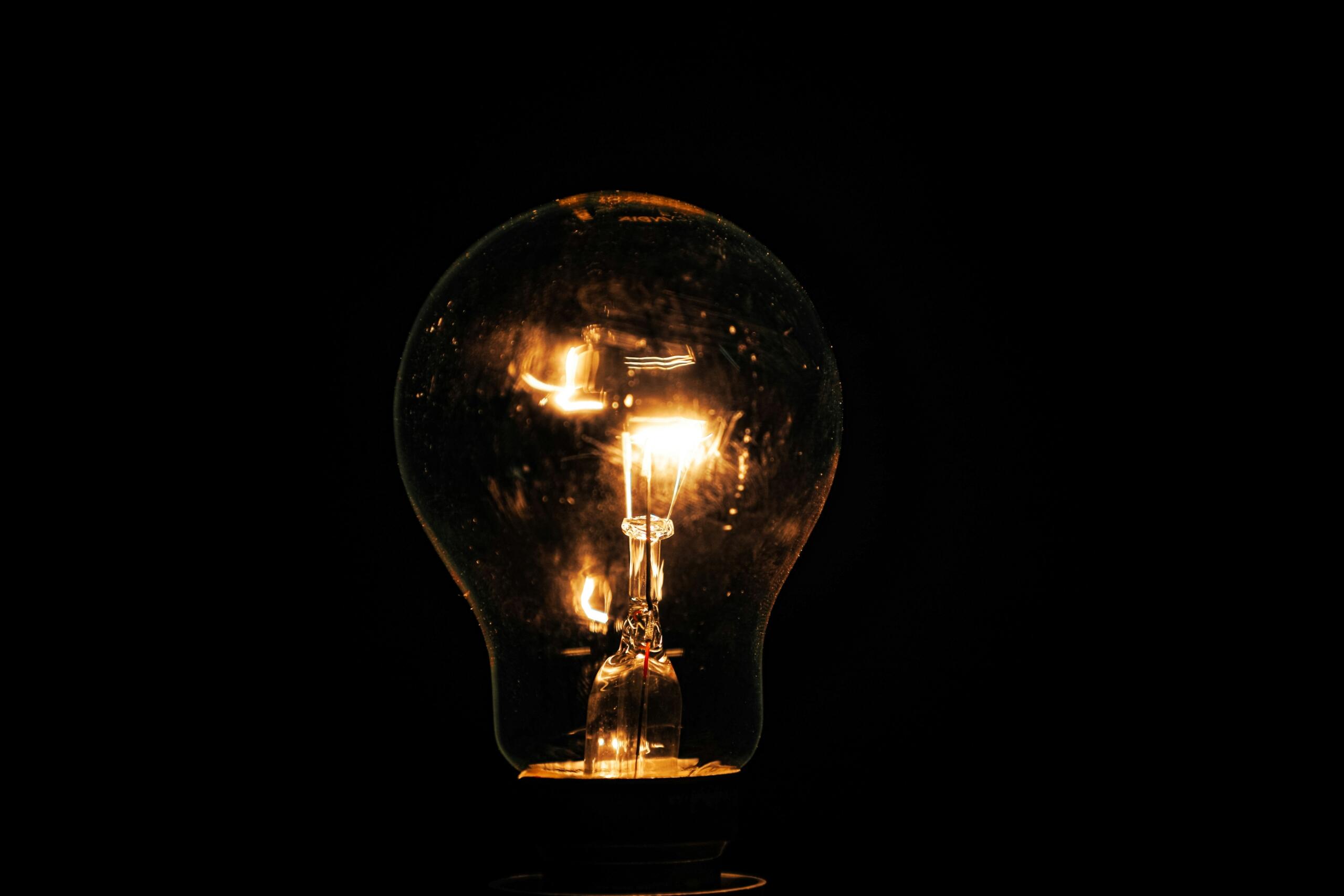 Una bombilla incandescente encendida con el filamento visible sobre un fondo negro.