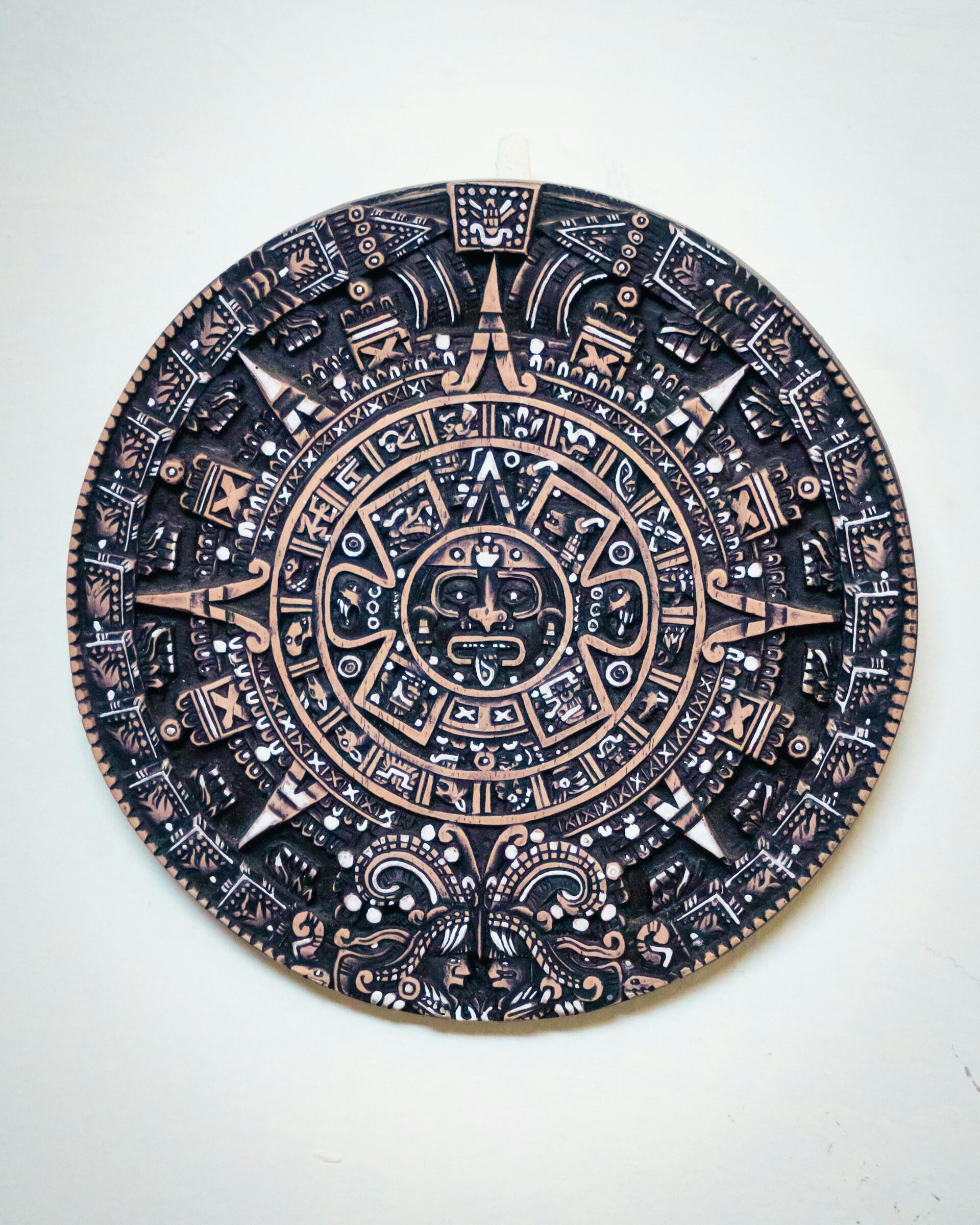 Intrincado diseño circular del calendario azteca con tallas detalladas en tonos oscuros sobre un fondo claro, que transmite una sensación de arte antiguo e historia.