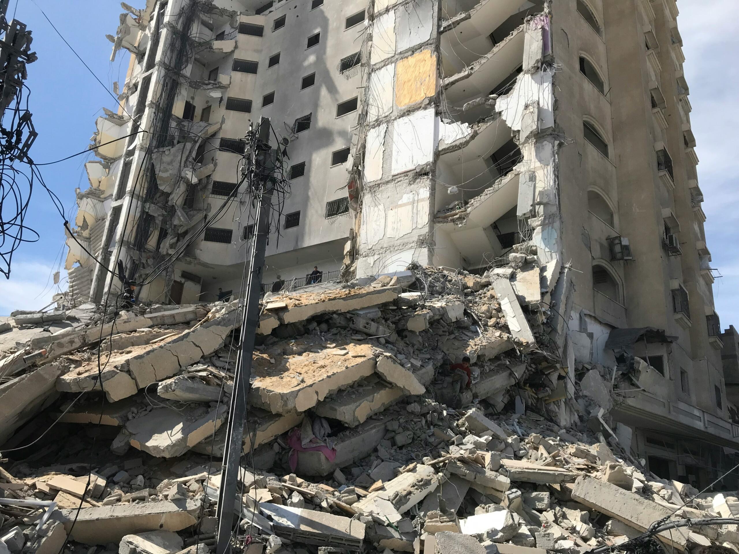 Edificio de varias plantas parcialmente derrumbado, con grandes escombros de hormigón y alambres retorcidos esparcidos a sus pies, bajo un cielo despejado.