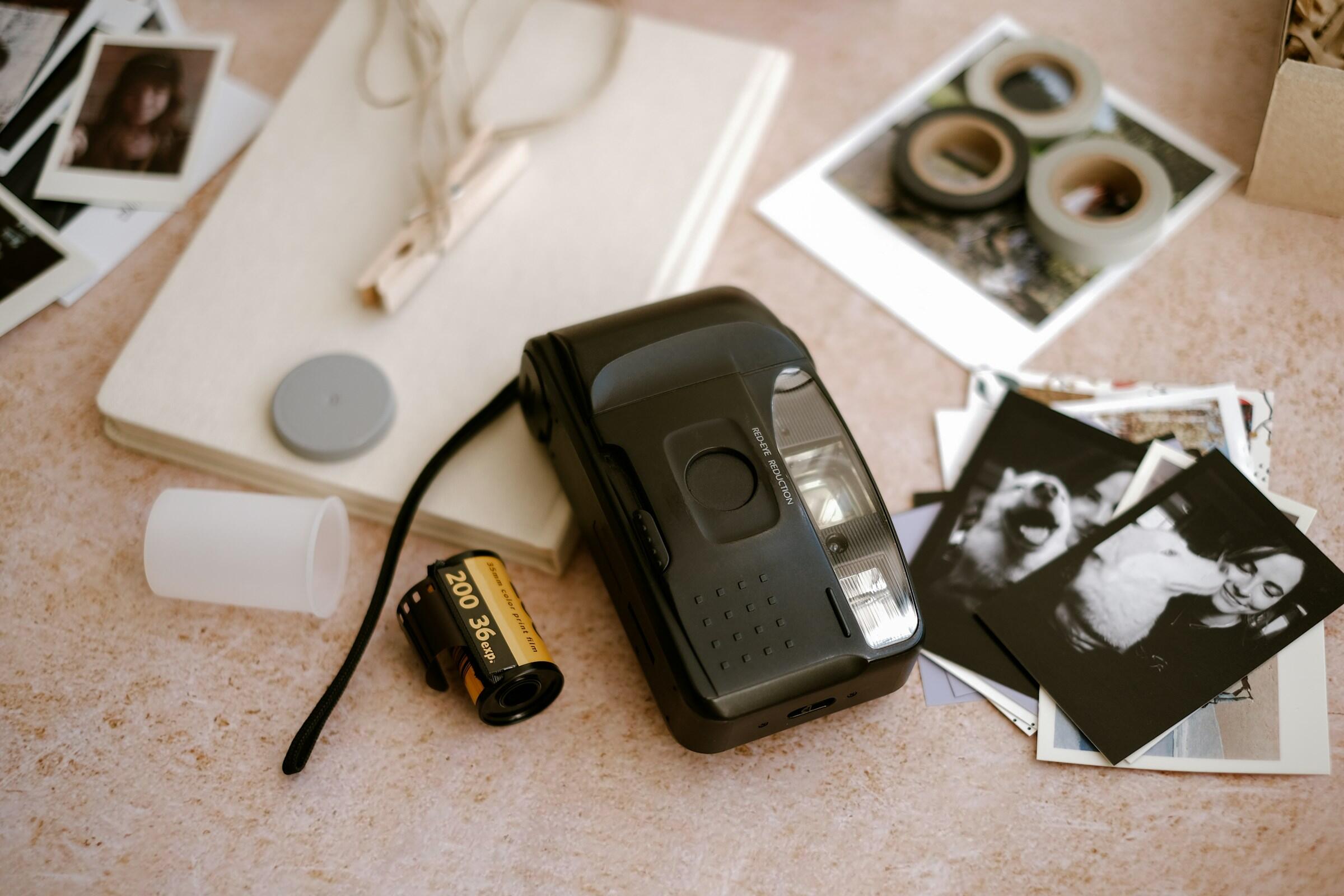 Cámara analógica con un rollo de película, fotos impresas, un cuaderno y cinta adhesiva fotográfica sobre una superficie texturizada.
