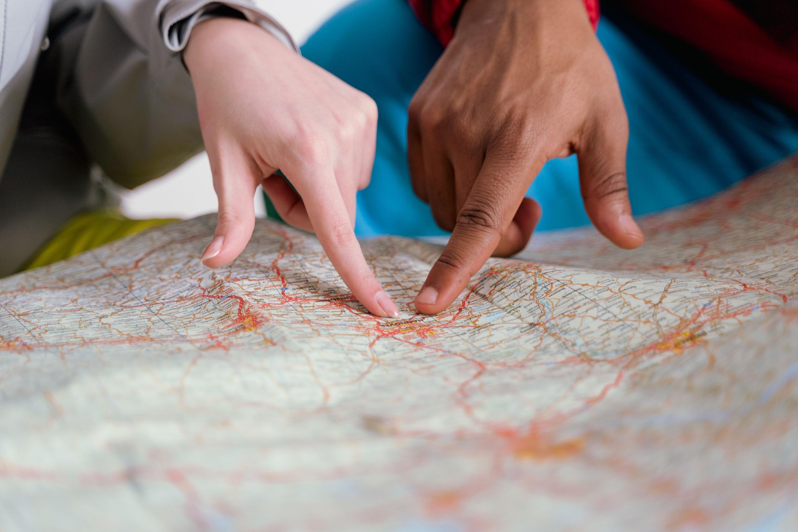 Los dedos de dos personas señalando distintos puntos en un mapa de carreteras detallado.
