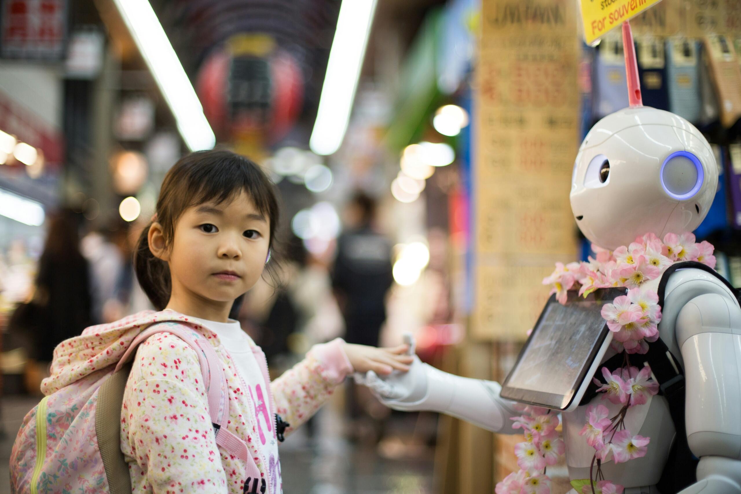 Una niña con una mochila va de la mano de un robot humanoide decorado con flores rosas y una tableta en un concurrido mercado cubierto.