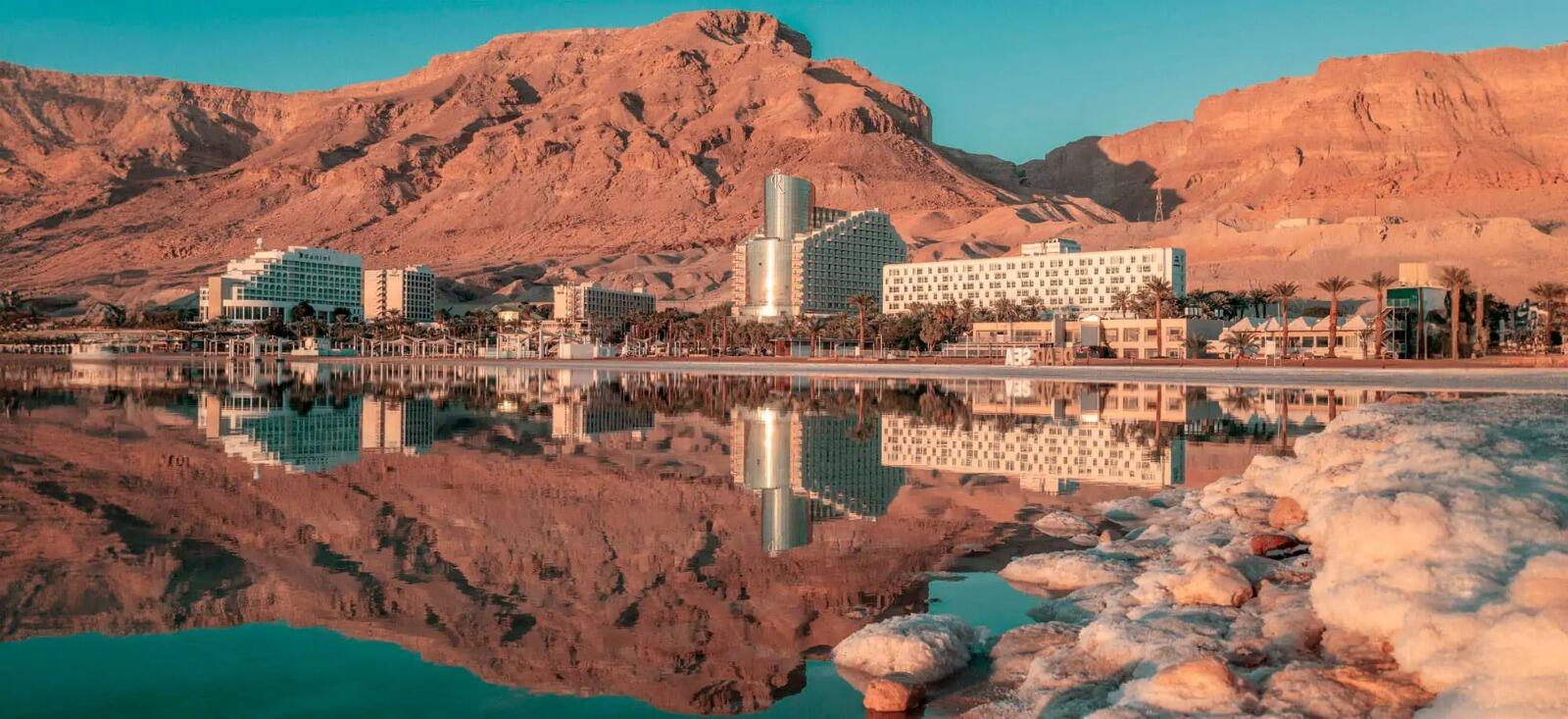 Paisaje desértico con edificios modernos reflejados en un lago en calma al atardecer. La escena transmite tranquilidad y contrasta la modernidad con la naturaleza.