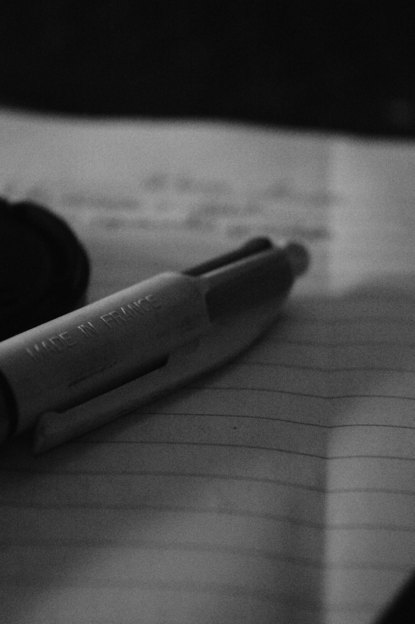 Una imagen en blanco y negro en la que se ve un bolígrafo con la inscripción «Made in France» apoyado sobre una página rayada de un cuaderno. La escena transmite un ambiente tranquilo y contemplativo.