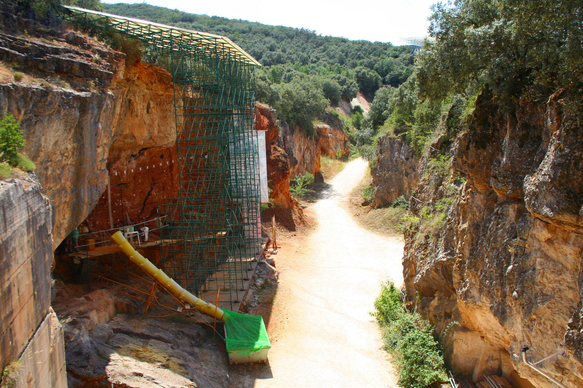 Yacimiento arqueológico de atapuerca en un cañón rocoso con andamios, cubiertas protectoras y un camino de tierra rodeado de vegetación.