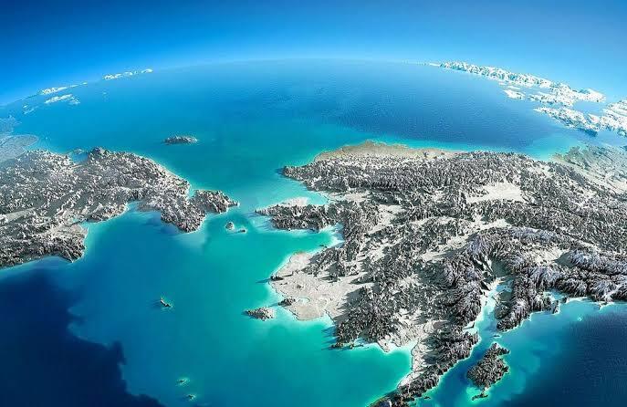 Vista aérea de una cordillera cubierta de nieve, rodeada de aguas de un turquesa intenso bajo un cielo azul claro, que transmite una sensación de inmensidad y tranquilidad.