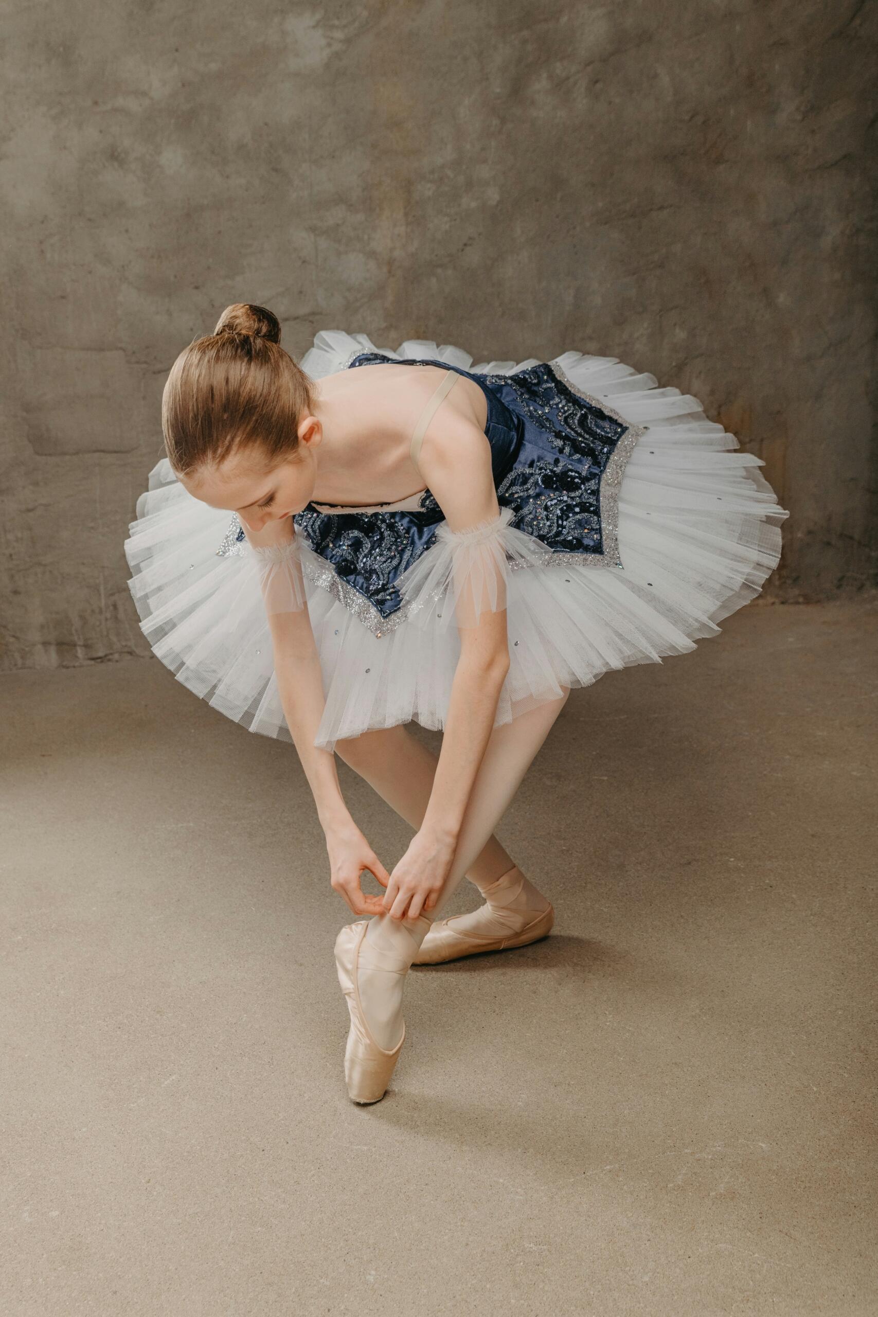 Bailarina de ballet ata sus zapatillas en un ambiente de tonos planos y parcos.