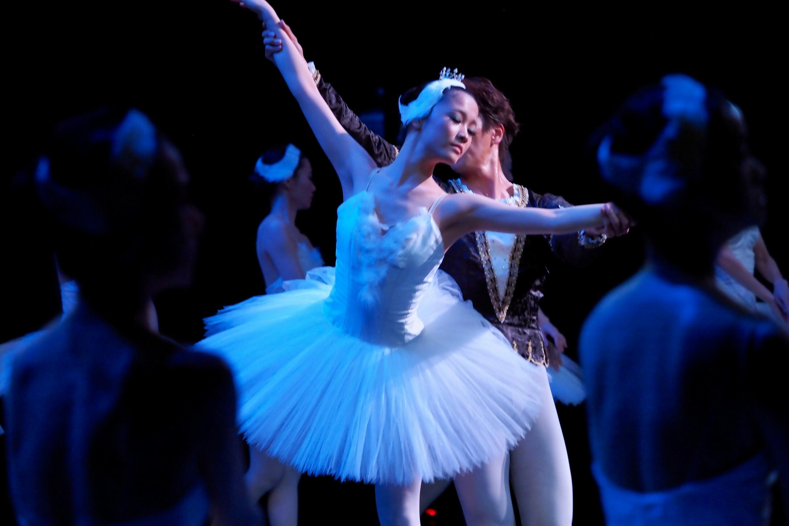 Bailarina danza ayudado por un bailarín en un escenario con el resto del elenco.