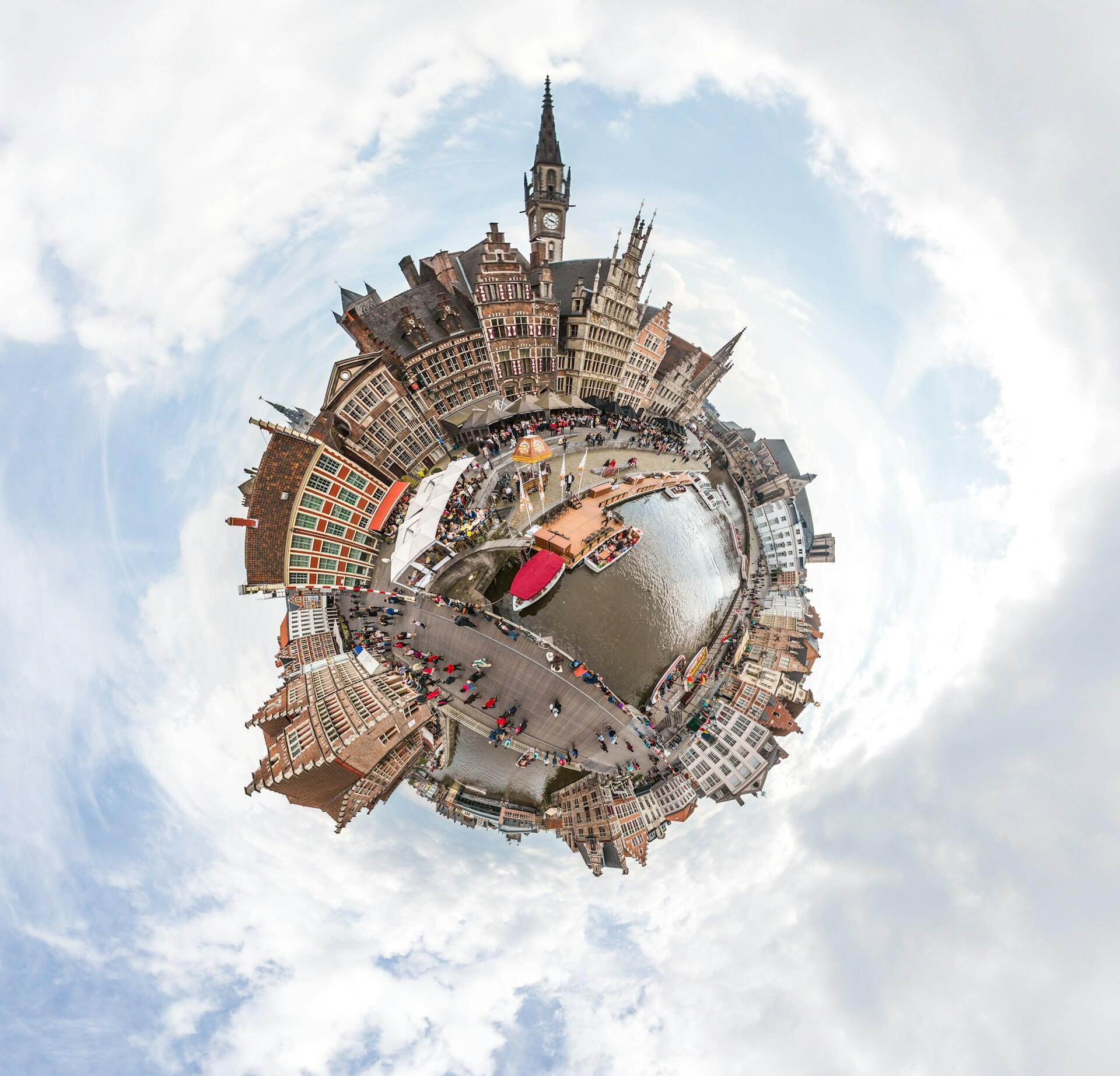 Vista en estilo «planeta en miniatura» de una histórica ciudad europea a orillas de un canal, con edificios antiguos, una torre del reloj, botes y multitudes bajo un cielo nublado.