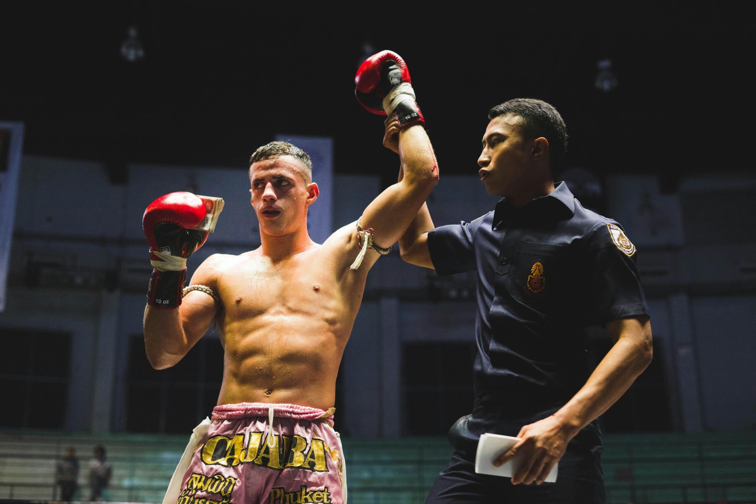 Un boxeador con guantes rojos fue declarado ganador por el árbitro en un ring con poca luz.