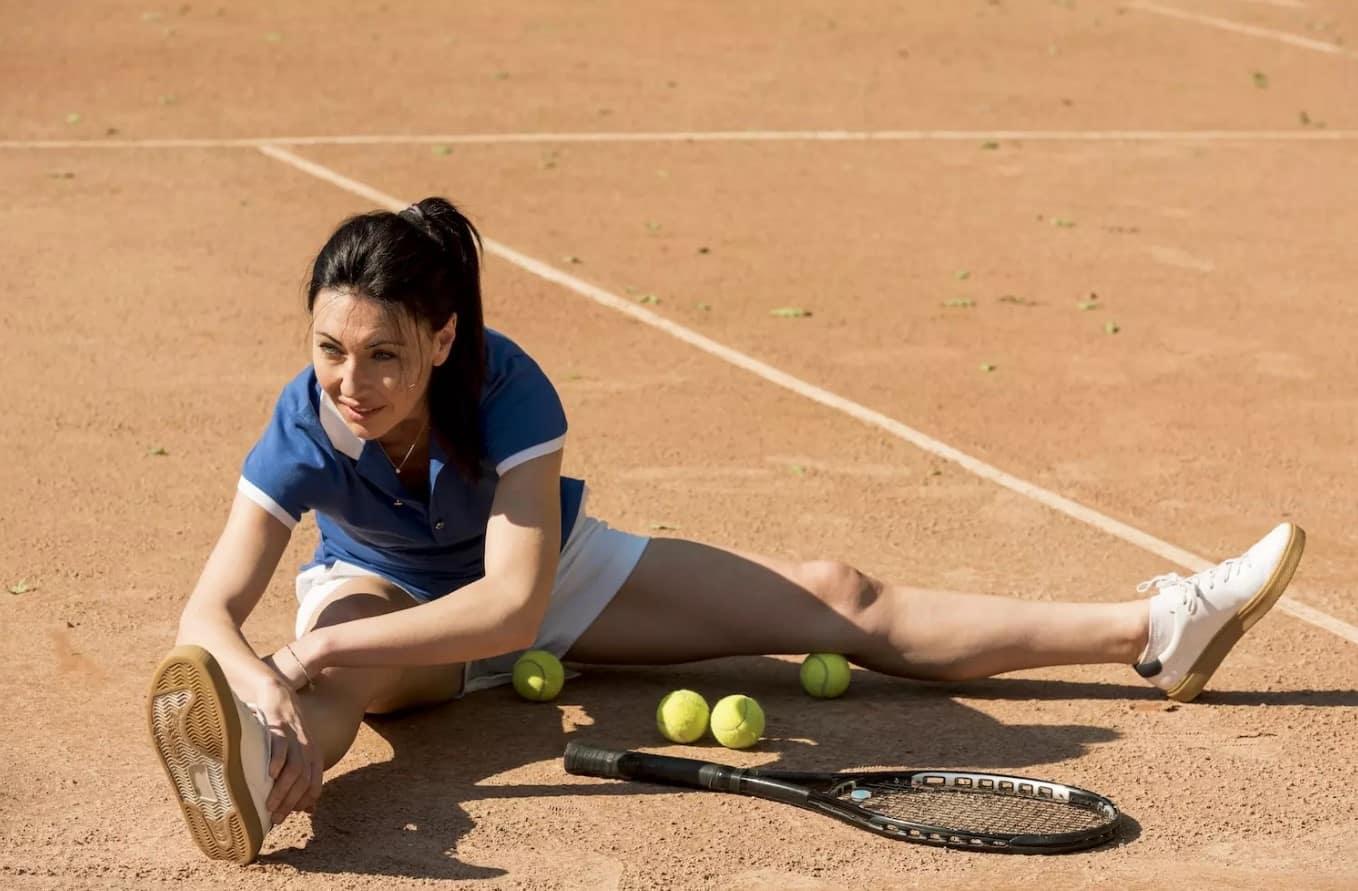 Mujer sentada en el suelo rodeada de pelotas de tenis, sonriendo y disfrutando del momento.