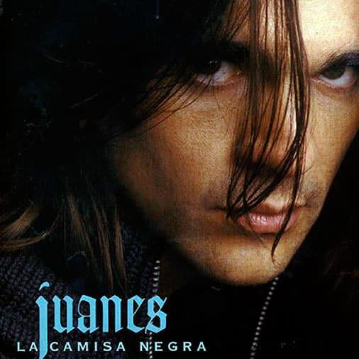 Primer plano de una persona de aspecto serio, con el pelo largo que le cubre parcialmente el rostro. En la parte inferior se lee «Juanes, La Camisa Negra» en letra azul.