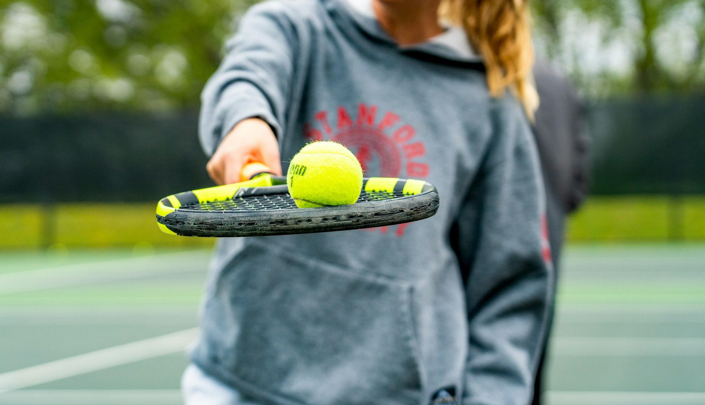 Mujer sosteniendo una raqueta de tenis y una pelota, lista para jugar en la cancha.