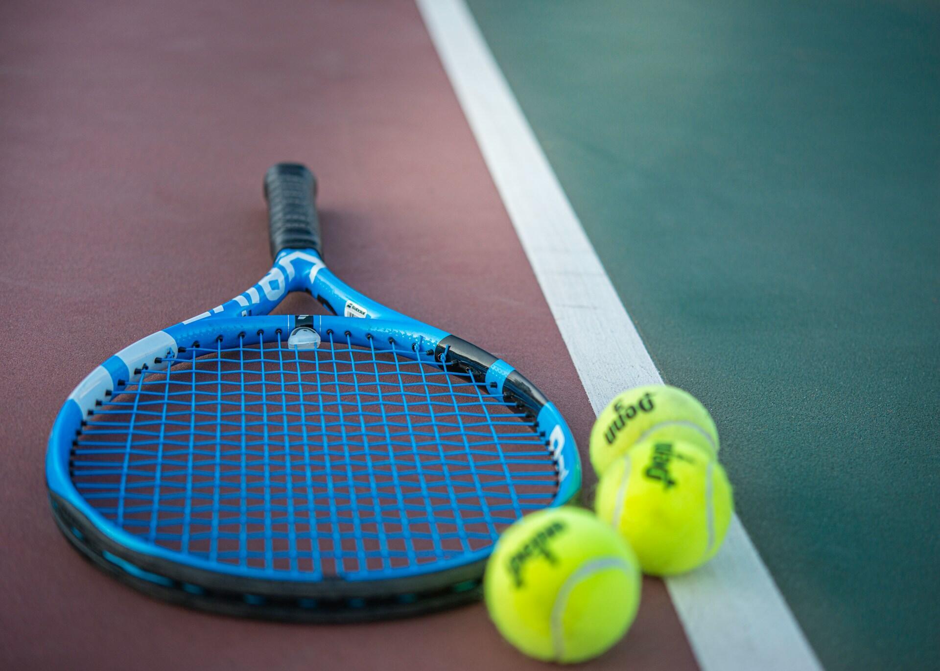 Una raqueta de tenis y dos pelotas reposan sobre una cancha de tenis.