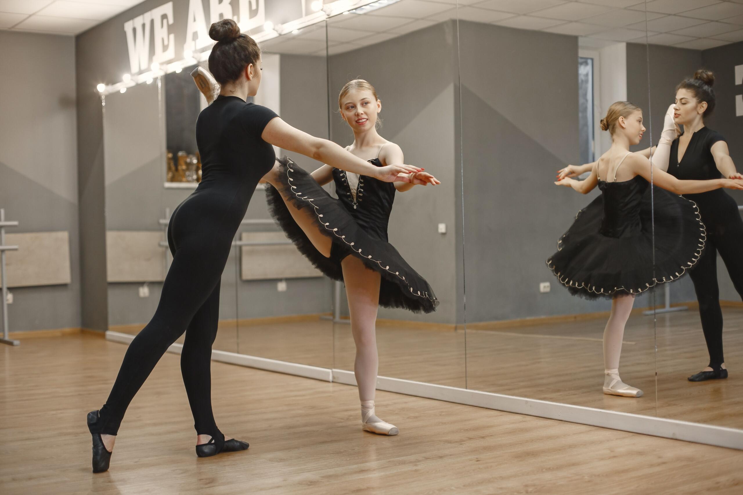 Bailarines de ballet practicando la técnica de puntas en un estudio, con reflejos en el suelo pulido.