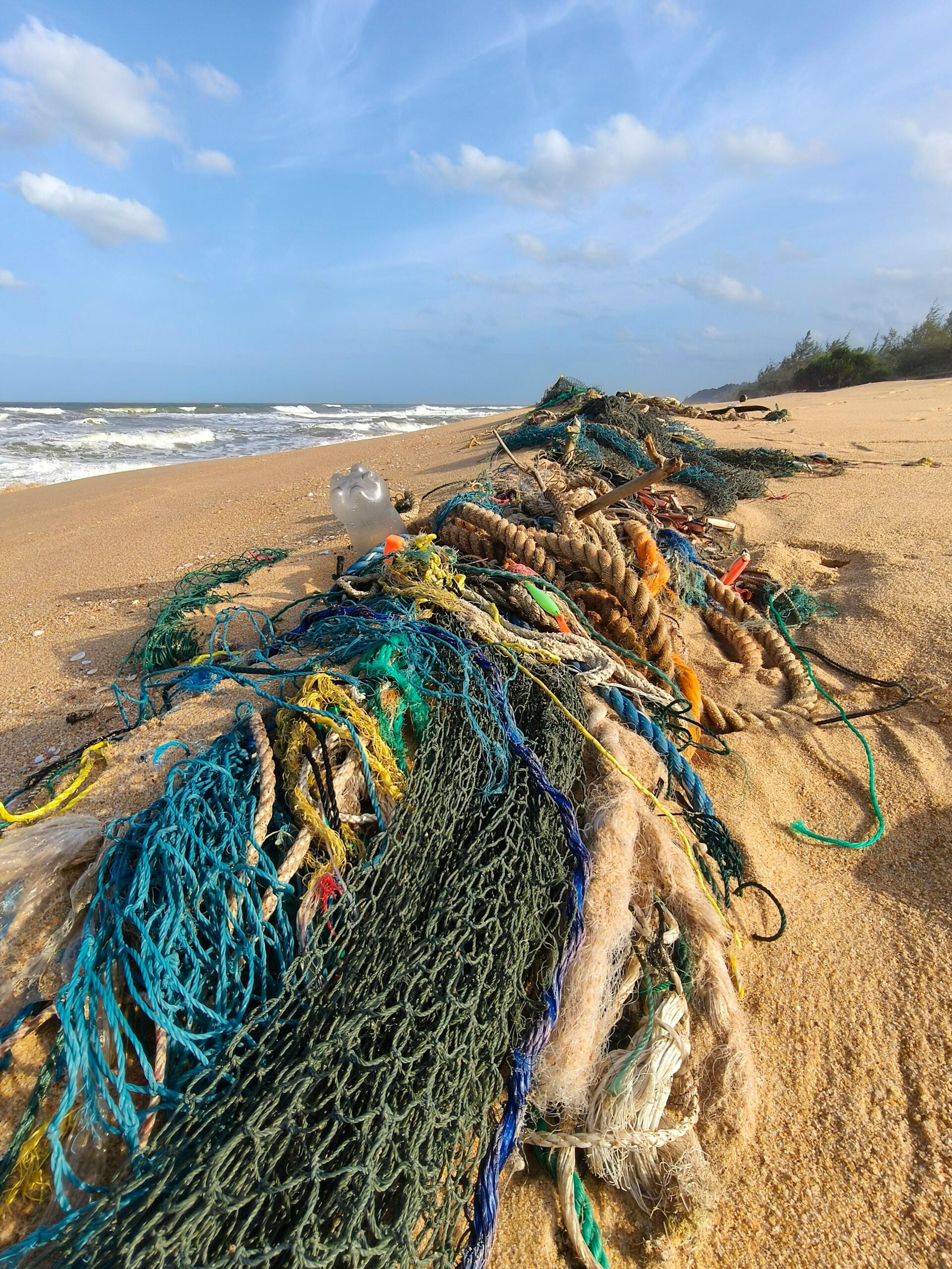 Redes de pesca enredadas, cuerdas y residuos plásticos yacen en una playa de arena junto a las olas del mar, lo que pone de relieve la contaminación marina y la preocupación medioambiental.