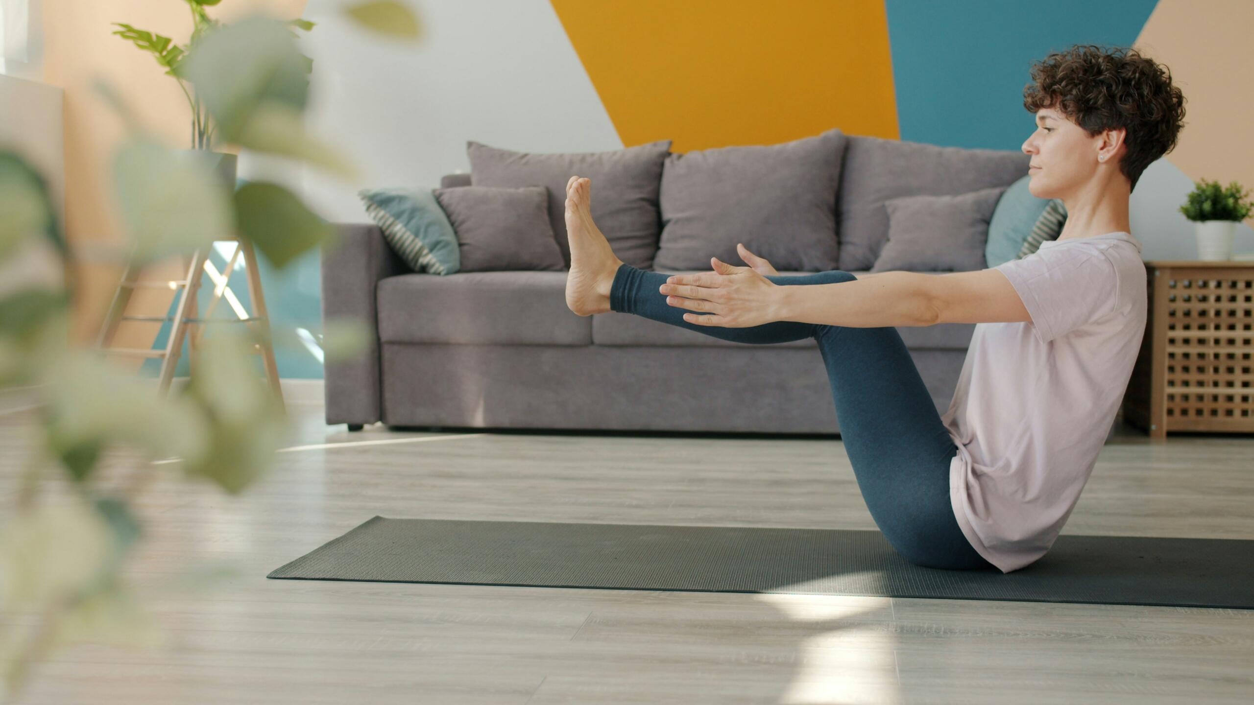 Una persona está arrodillada sobre una esterilla de yoga, estirando la pierna de otra persona en un salón muy luminoso.