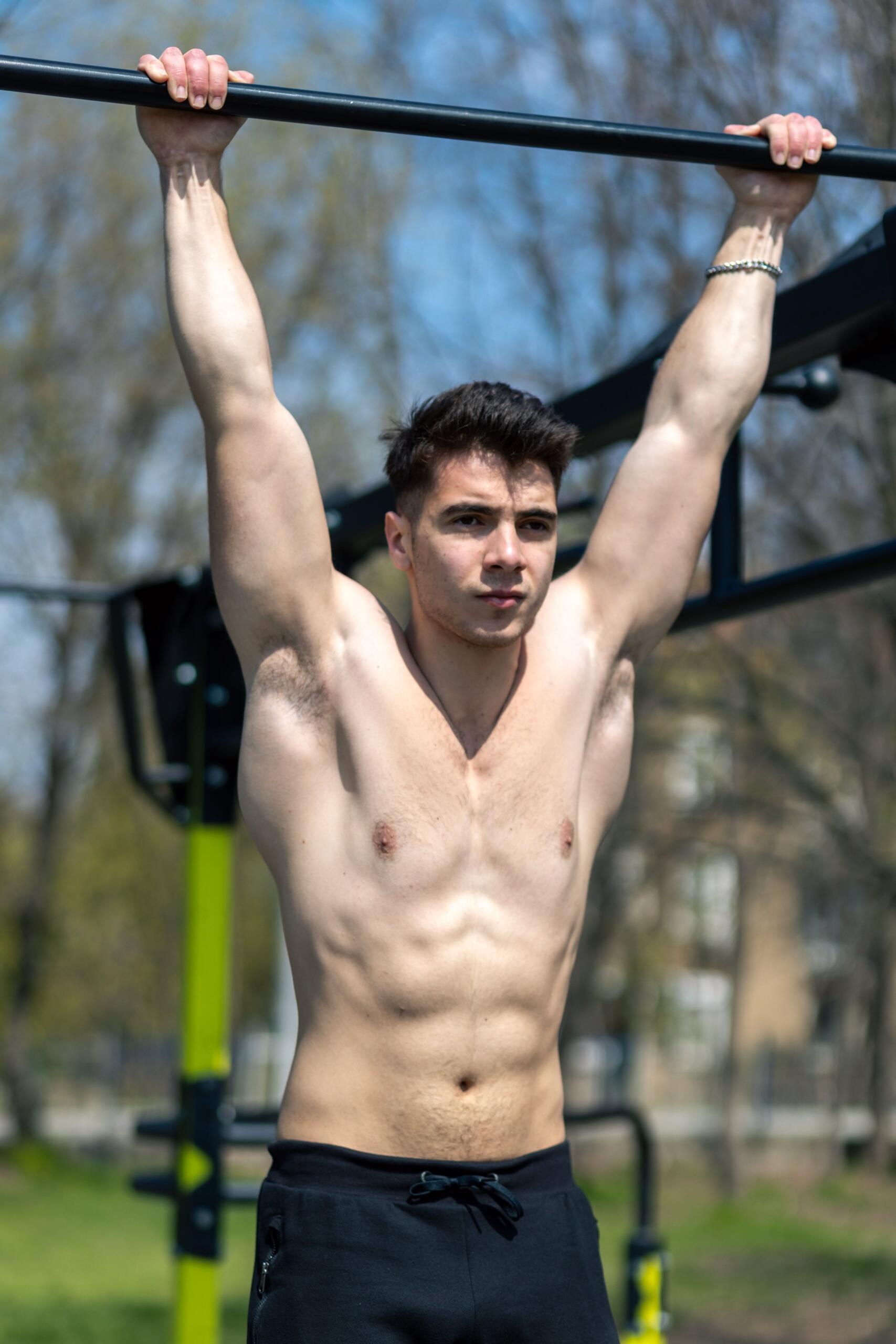 Hombre musculoso haciendo una dominada en una barra horizontal en un gimnasio.