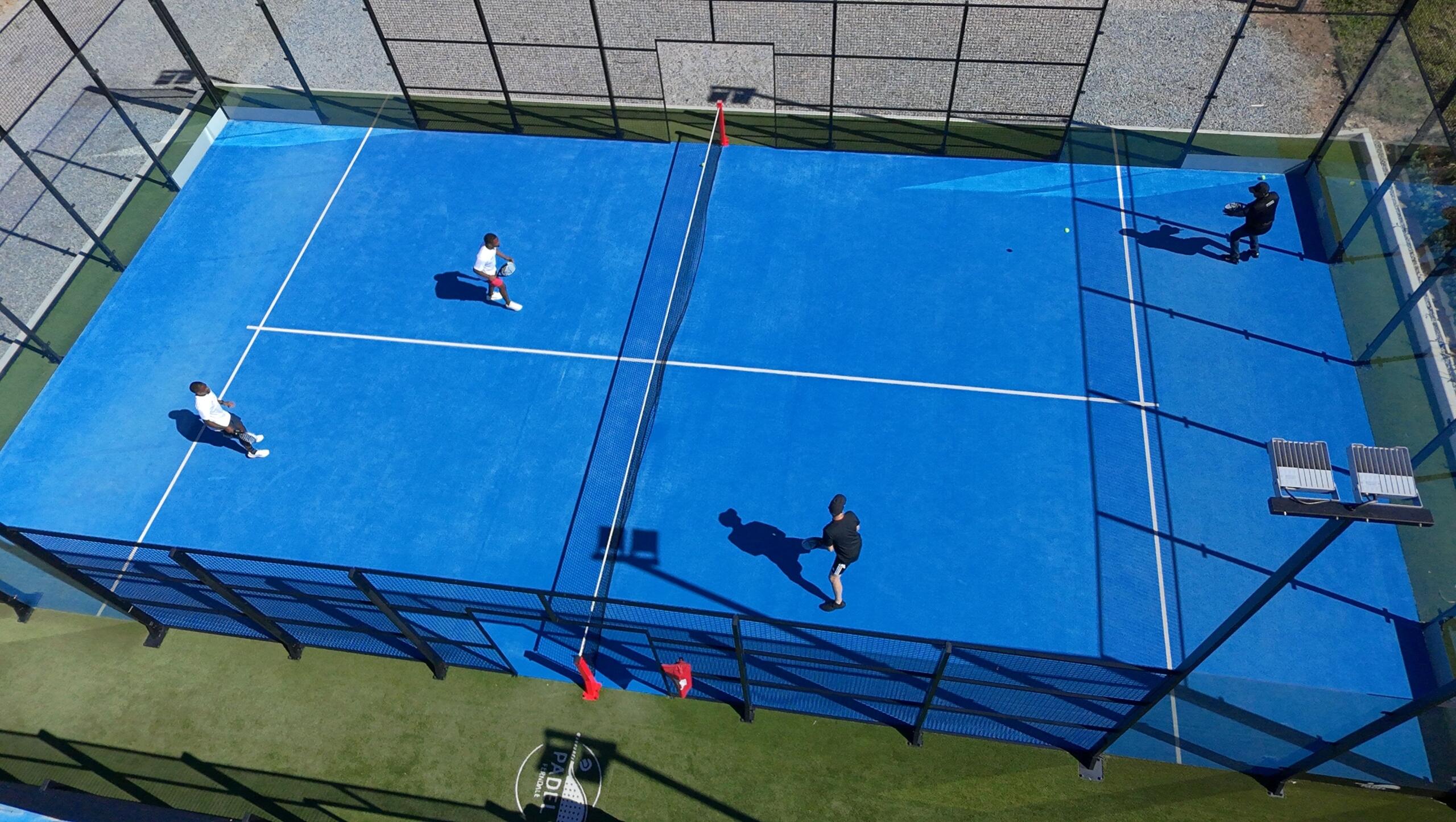 Vista aérea de los jugadores compitiendo en una pista de pádel de color azul brillante rodeada por una valla.