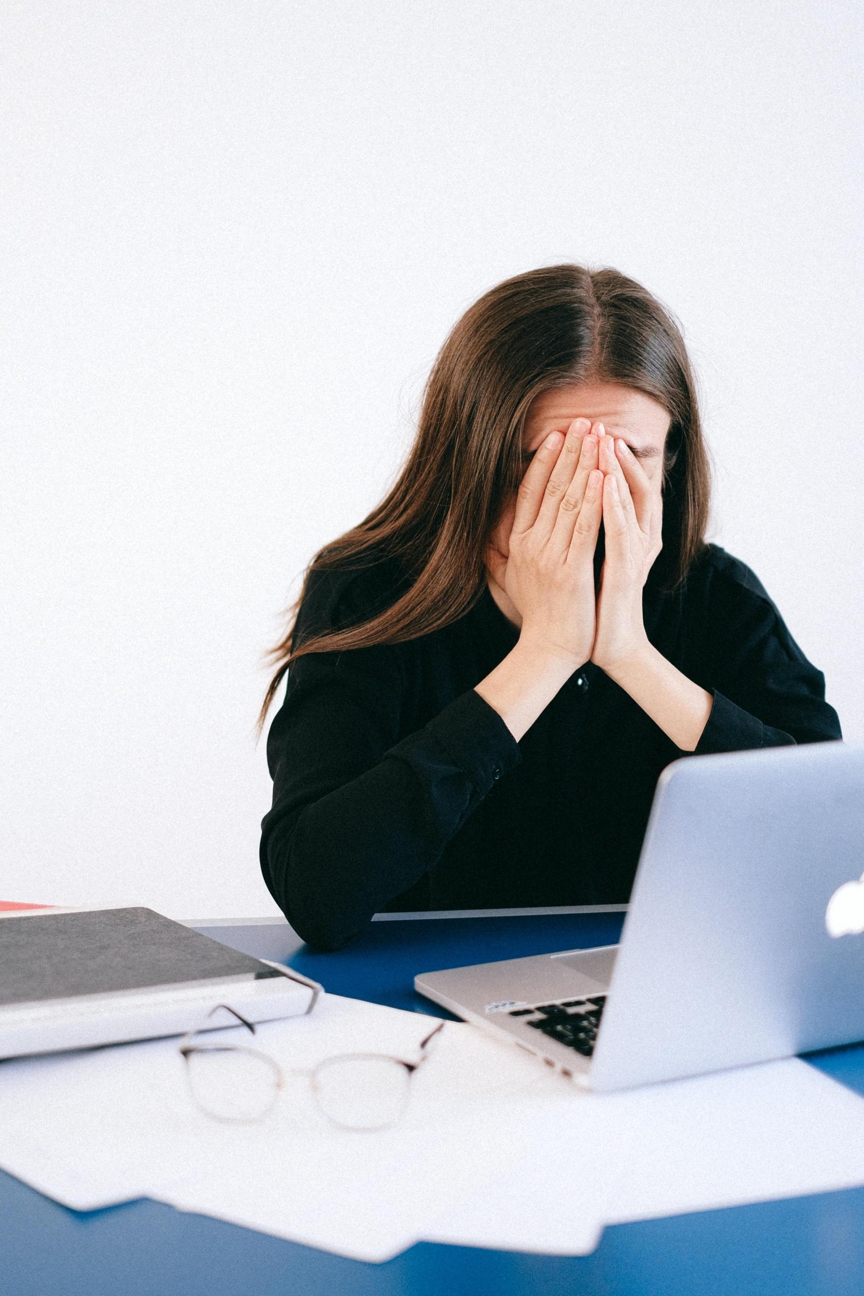 Tyttö istuu stressaantuneena työpöydän ääressä kasvot haudattuina käsiin.